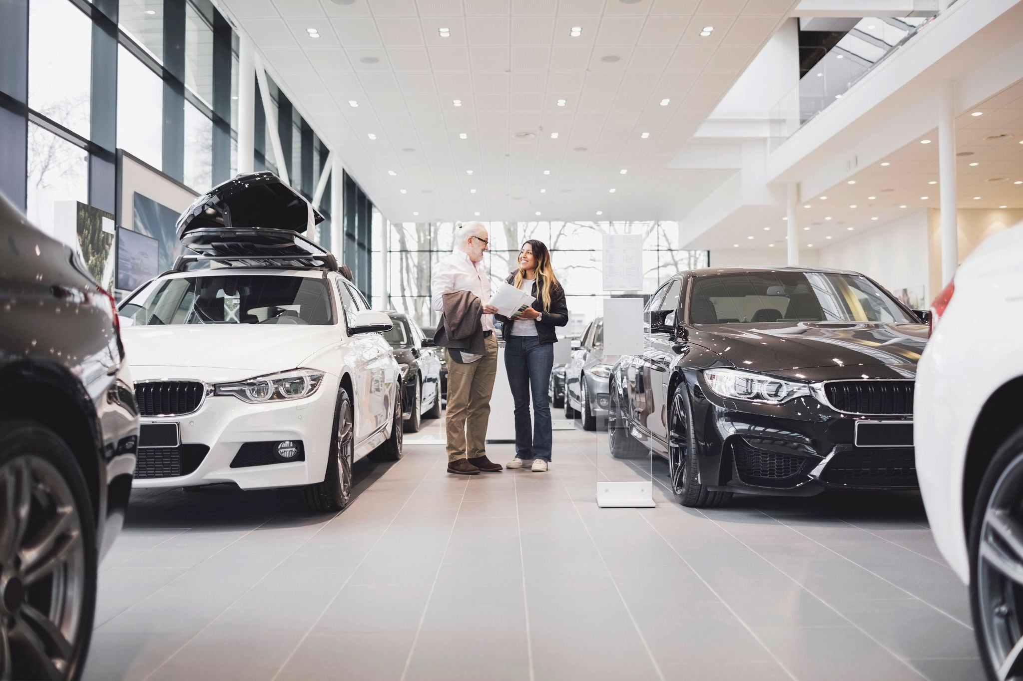 Man woman paperwork standing amidst cars showroom