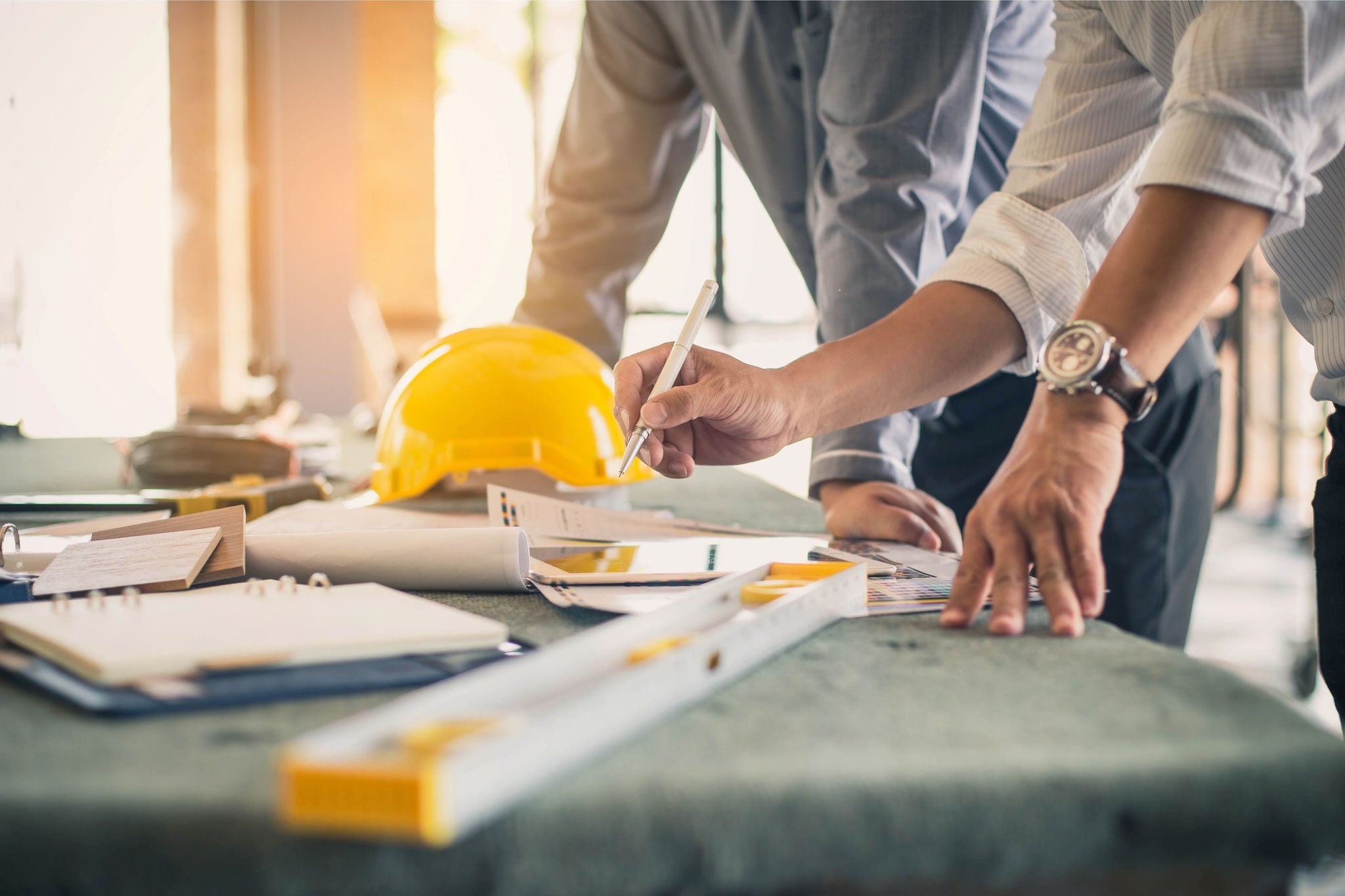 People working on a construction plan with a yellow helmet on the table