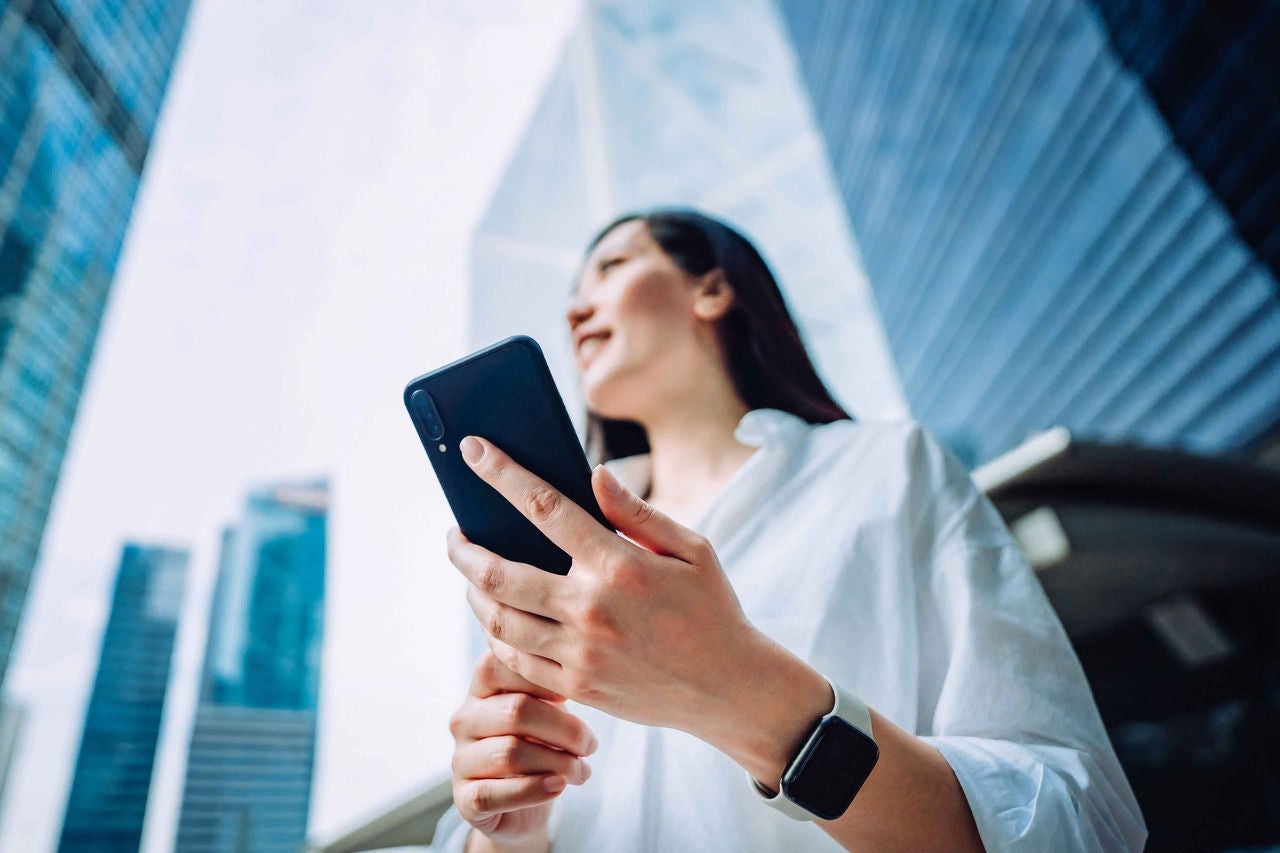 Frau mit einem Smartphone in der Hand vor Wolkenkratzern