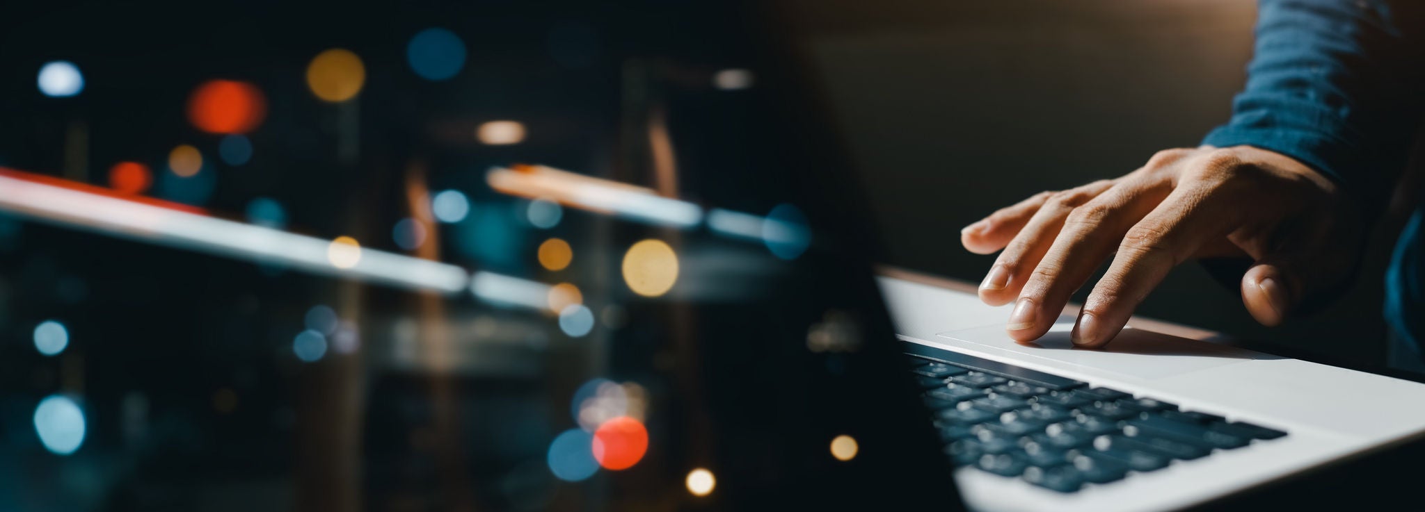 young man hand working on a laptop, bokeh blurred at night For text copy space, image size horizontal