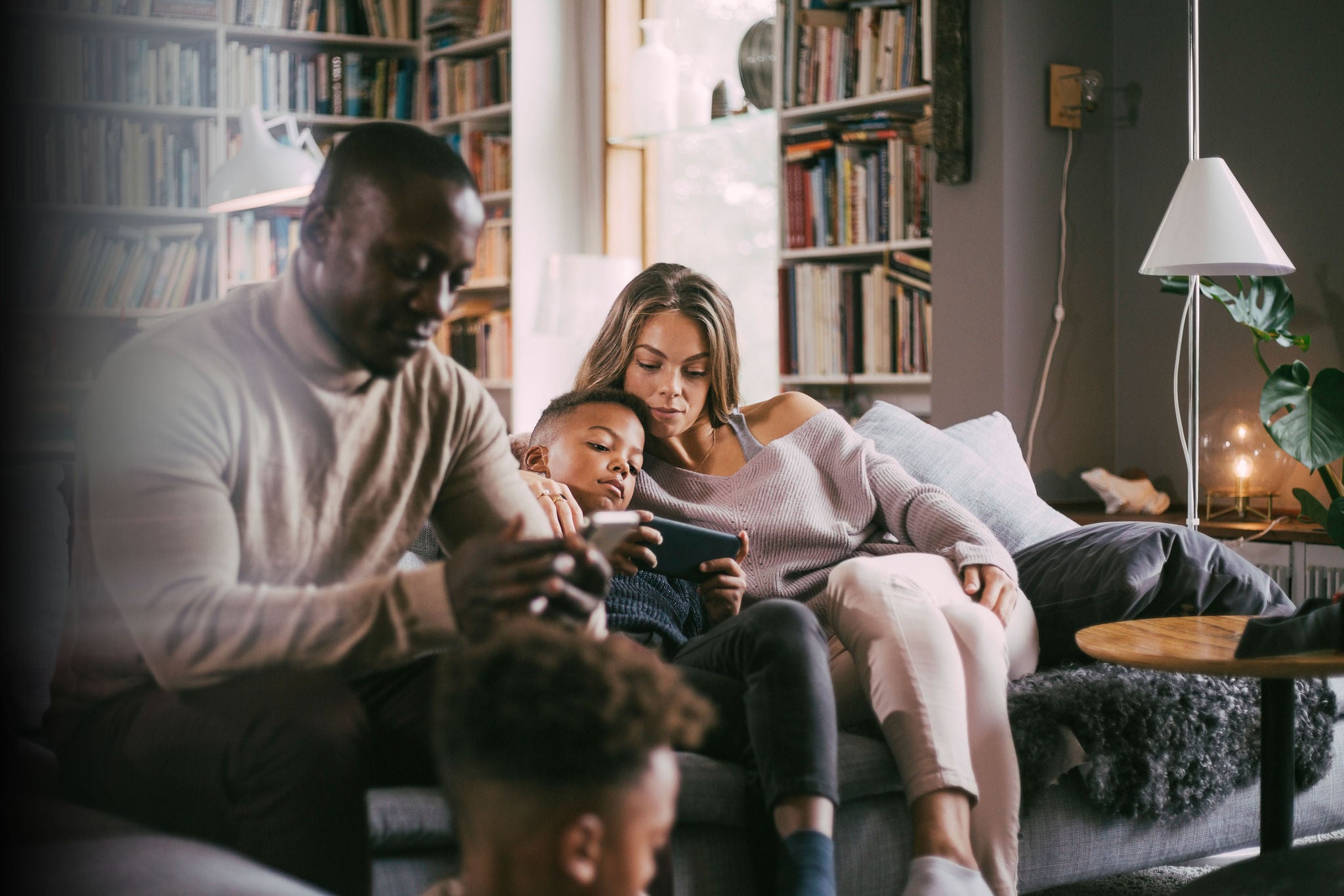 A family sitting on a sofa in a cozy living room, using a smartphone together.