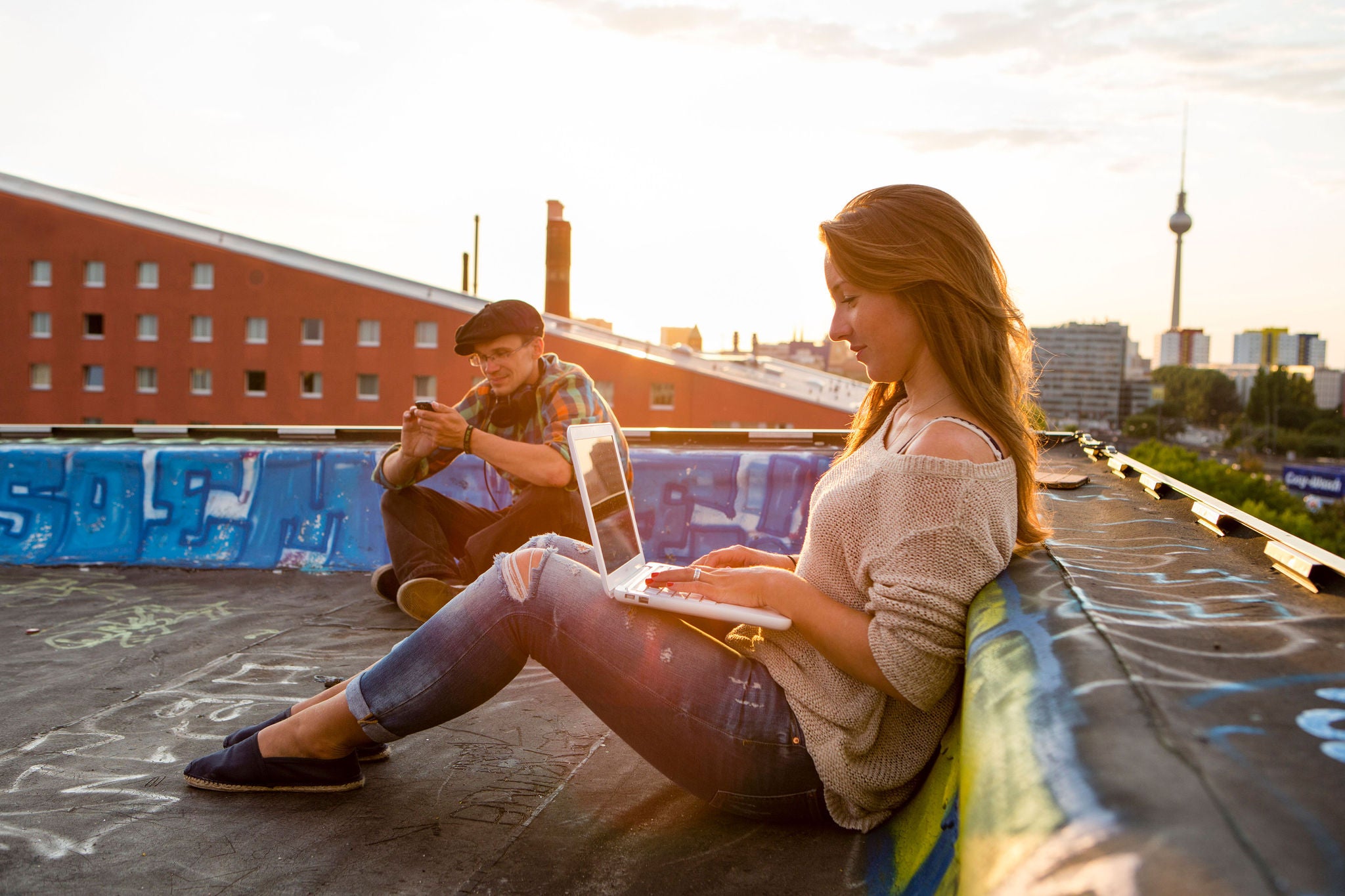 young woman sitting on a roof in Berlin and works at her laptop, in the background the skyline from Berlin with the television tower