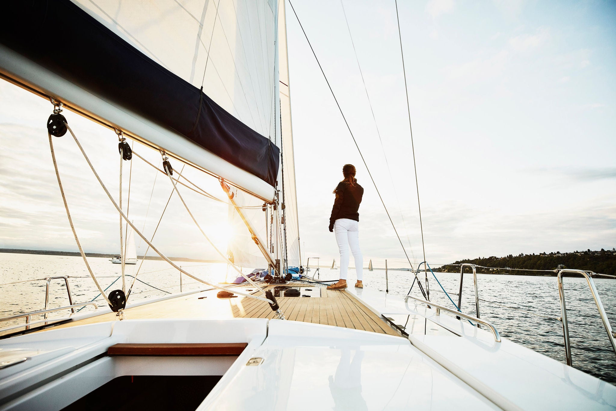 woman stands foredeck sailboat watching sunset summer evening