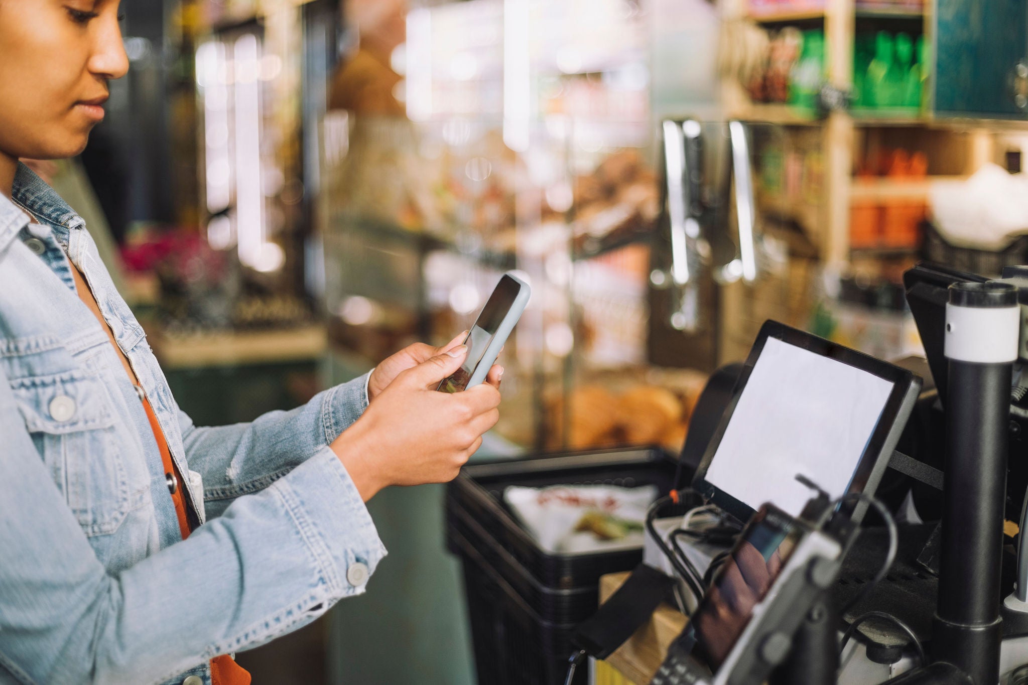 Woman using smart phone while scanning QR code for payment at store checkout