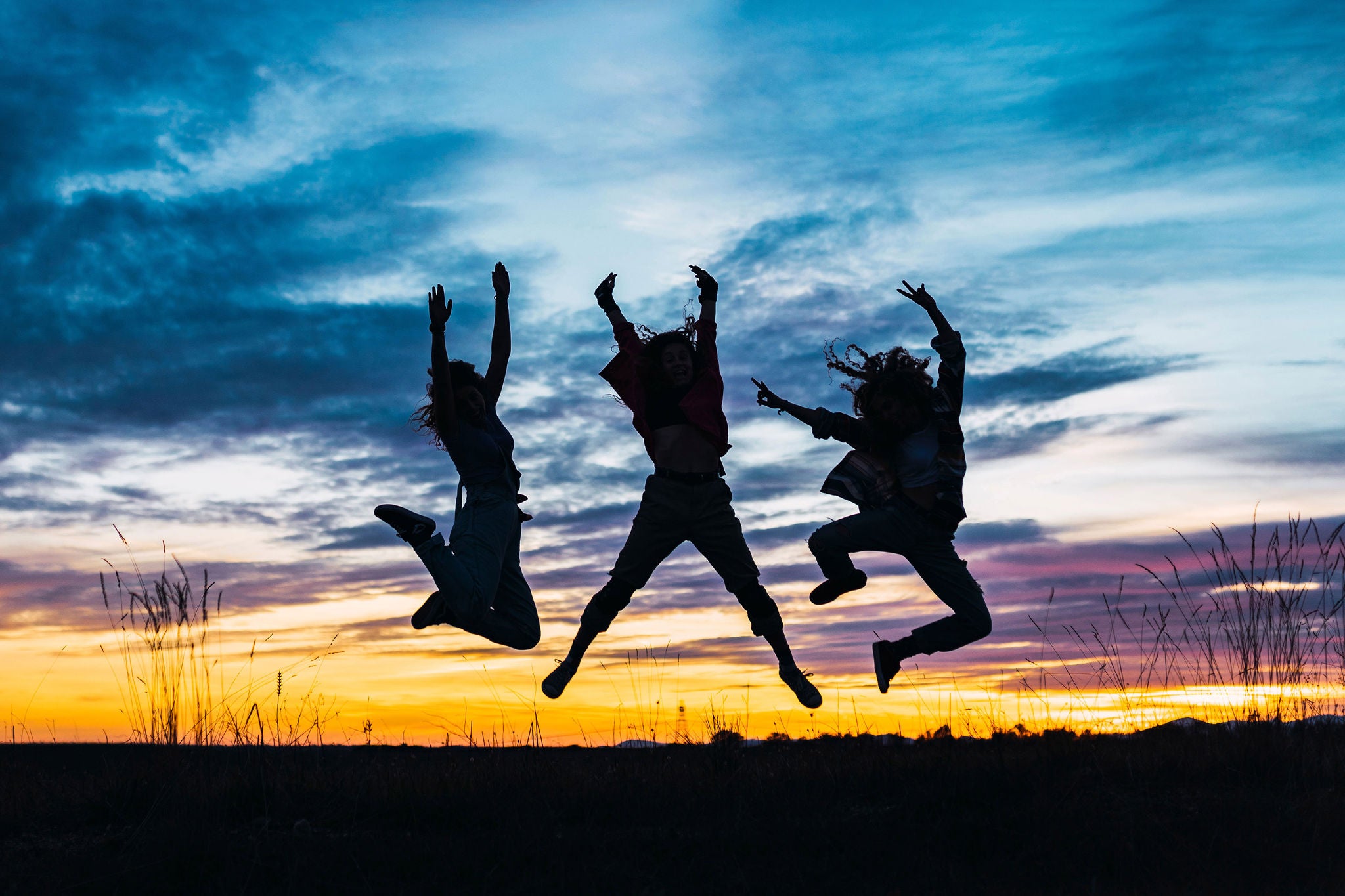 Carefree female friends with arms raised jumping in front of sky