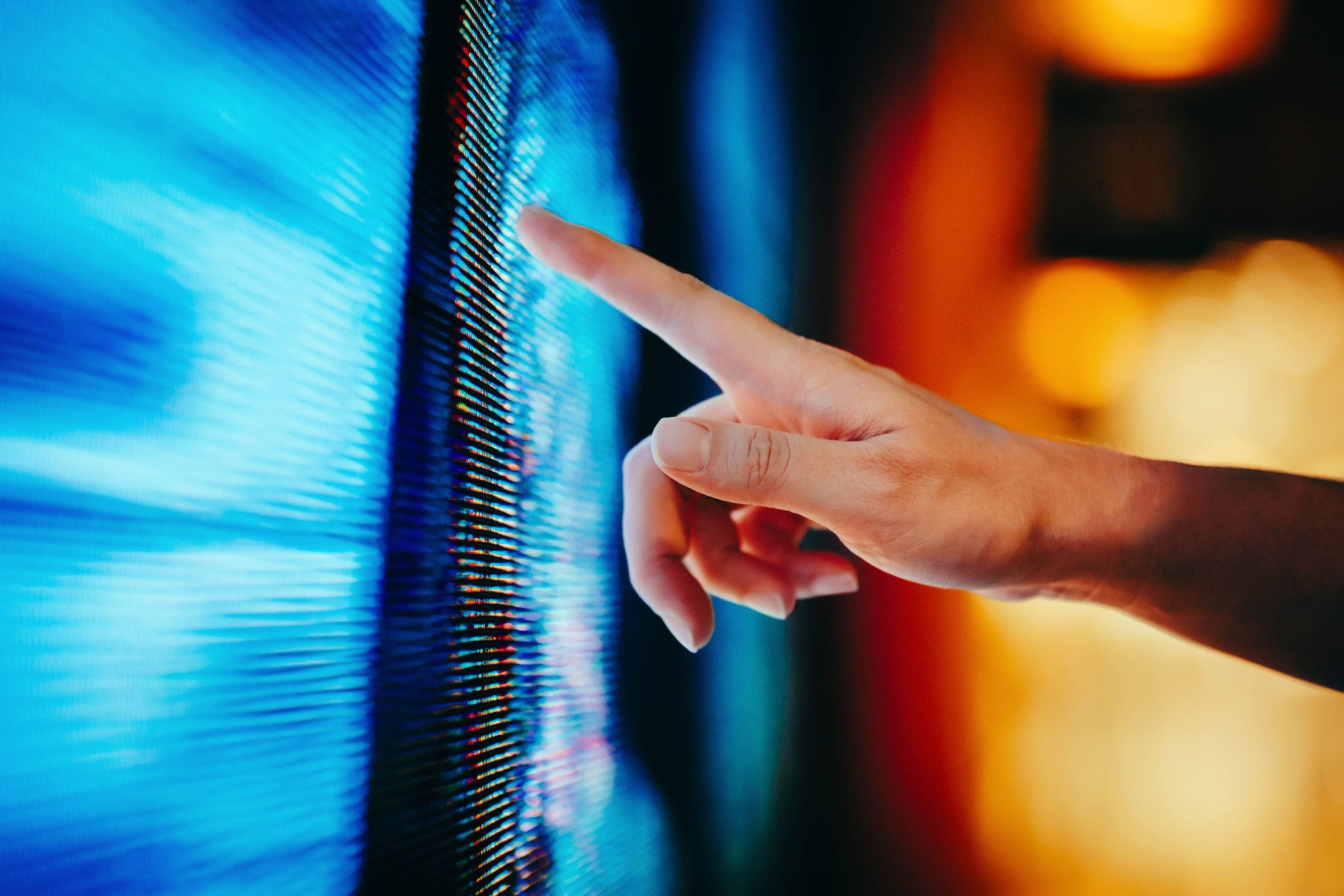 Close up of woman's hand touching illuminated and multi-coloured LED display screen, connecting to the future. People, lifestyle and technology