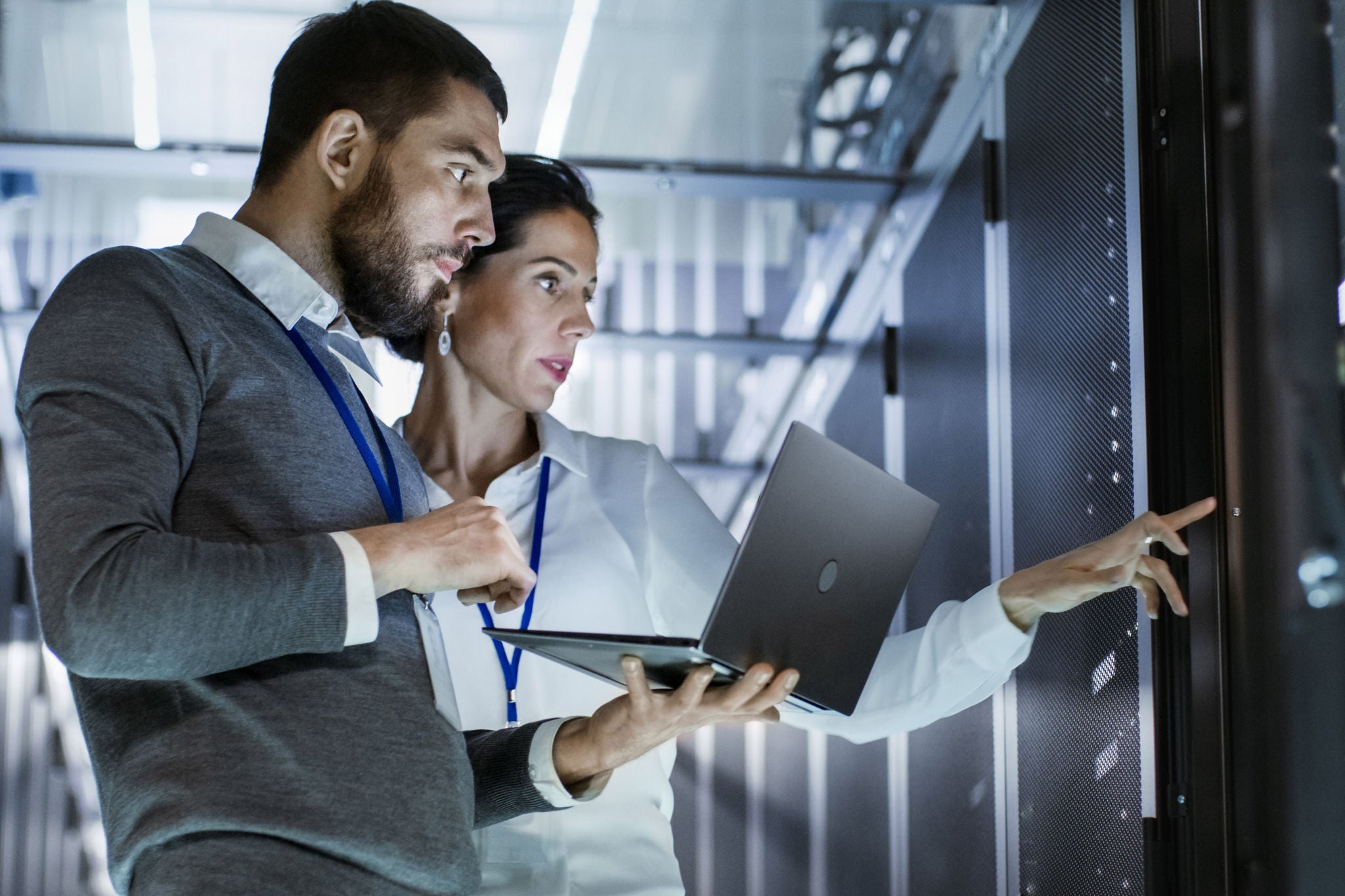 Male IT Specialist Holds Laptop and Discusses Work with Female Server Technician. They're Standing in Data Center, Rack Server Cabinet is Open.