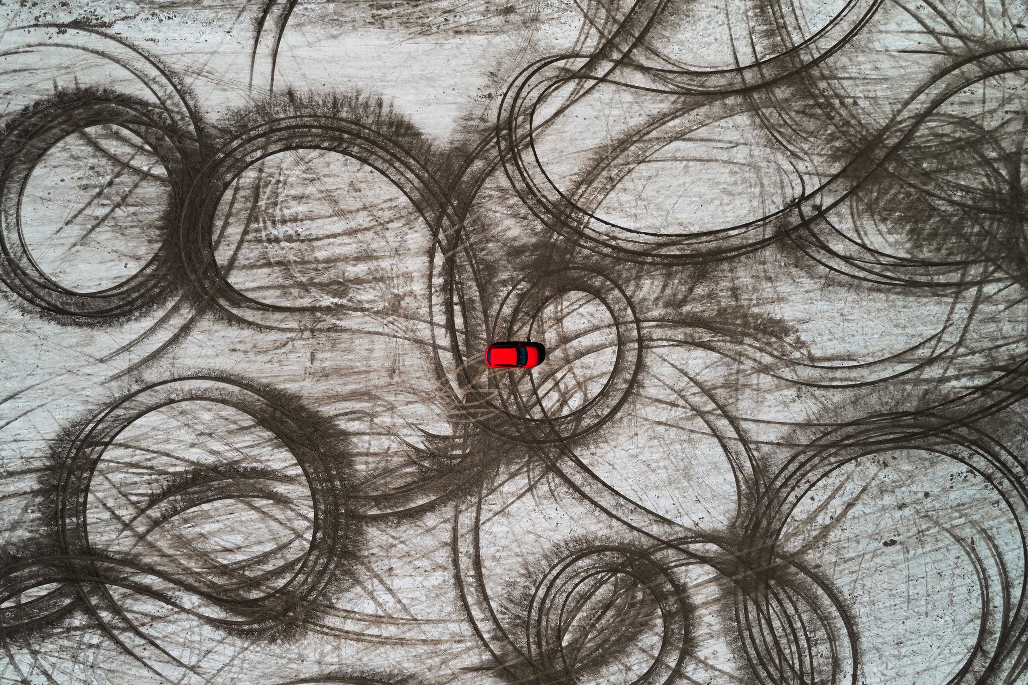 Red car and tire imprints on a beach as seen from above