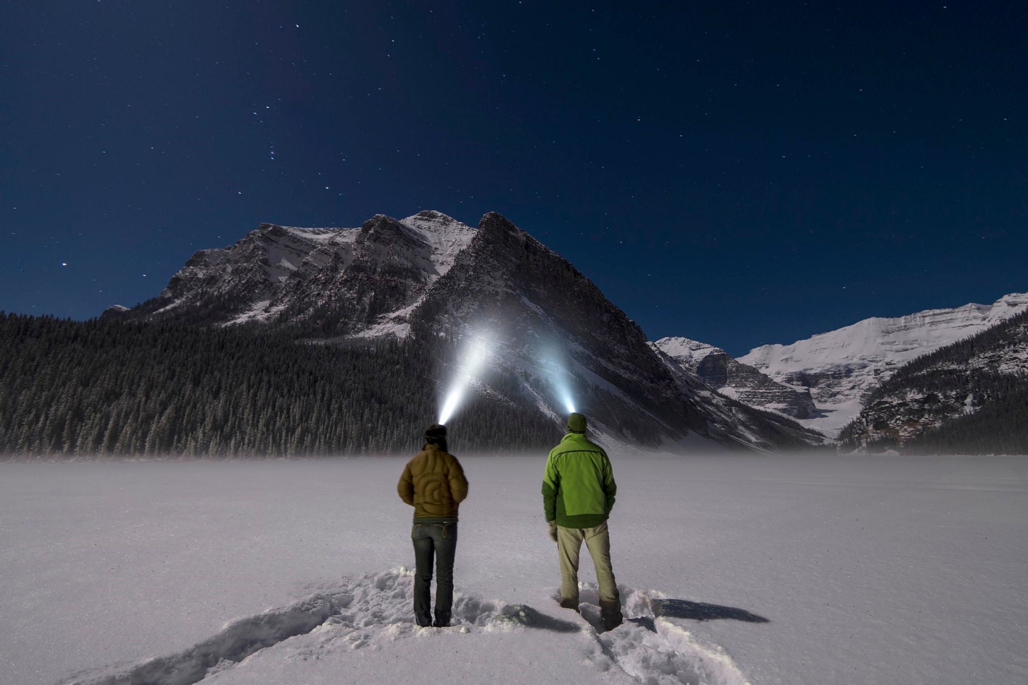 Deux personnes regardent une montagne à l’aide de lampes frontales