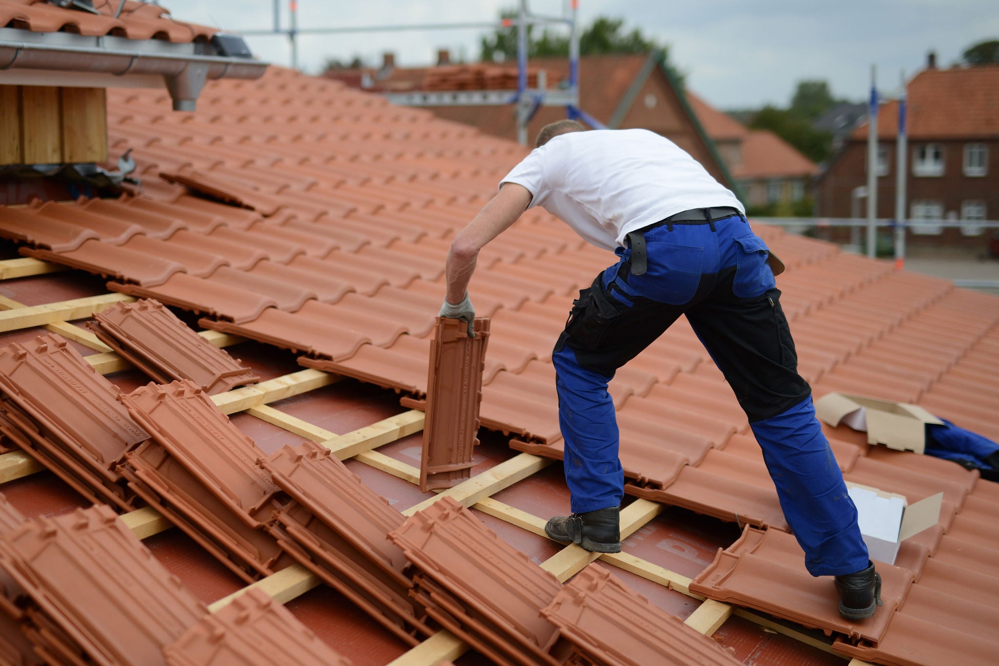 Dachdecker mit weissem T-Shirt auf dem Dach eines Hauses und einer Dachbaustelle