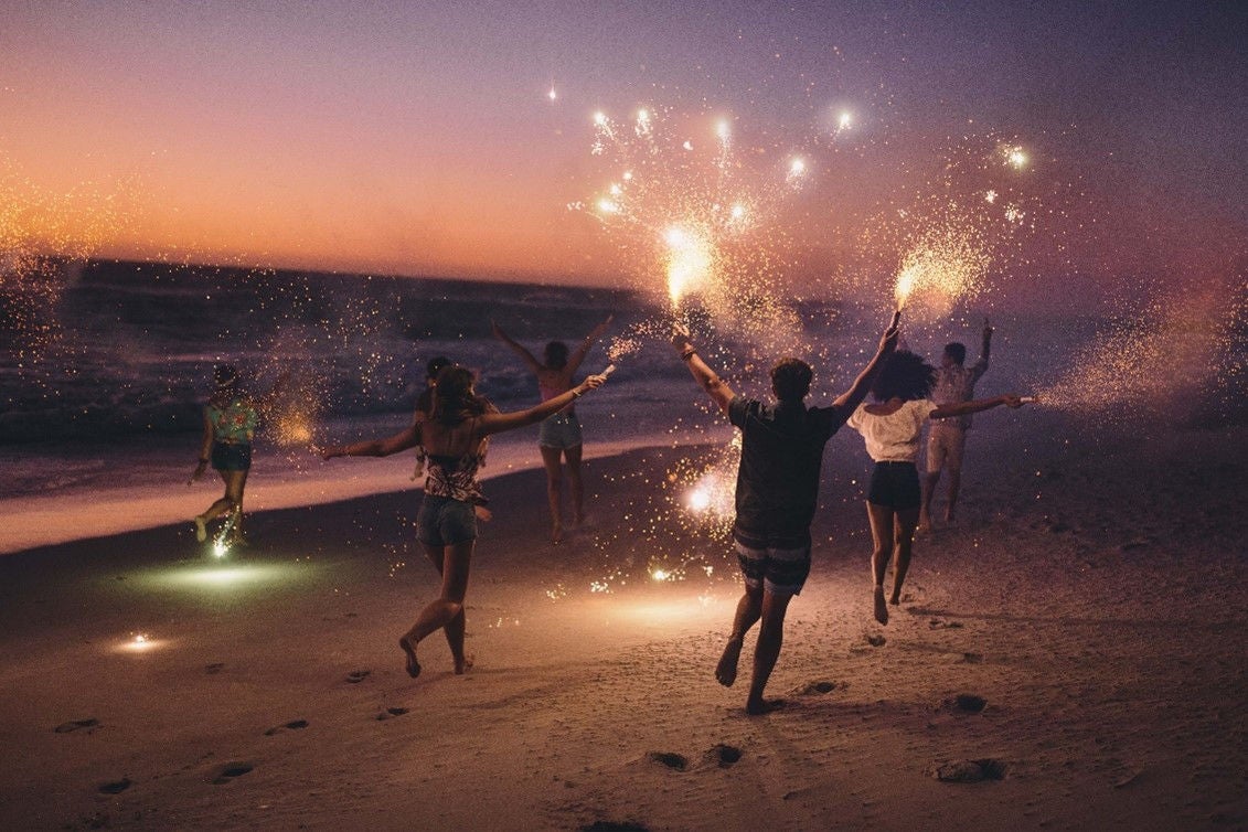 Des gens avec des cierges magiques sur la plage la nuit.