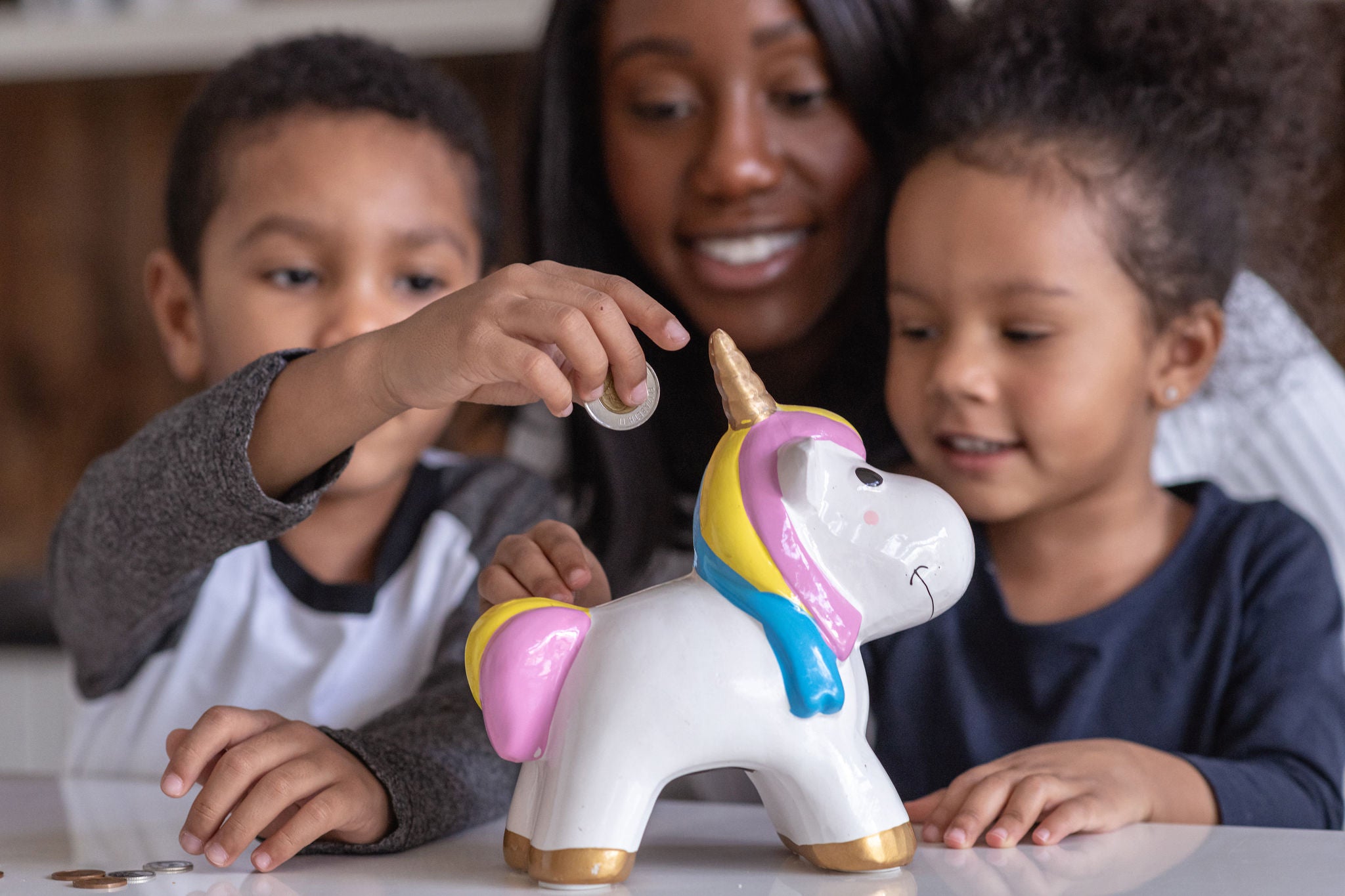 Une mère d'origine afro-américaine enseigne à ses deux enfants en âge de fréquenter l'école primaire l'importance d'économiser de l'argent pour un avenir meilleur. Les adorables enfants ajoutent tout leur argent de poche à la tirelire en forme de licorne.