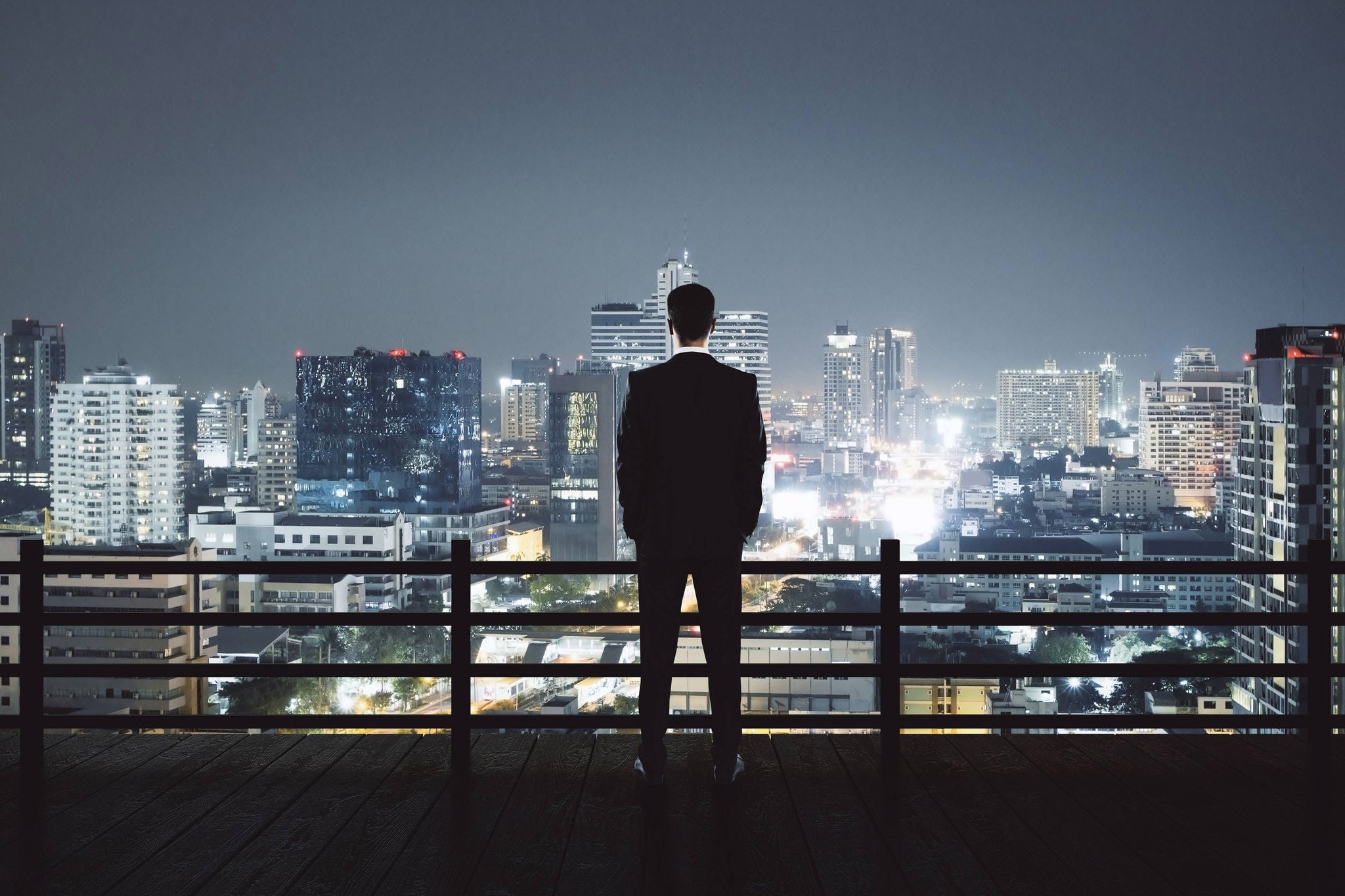 Back view of young businessman on rooftop looking at illuminated night city. Research and success concept 