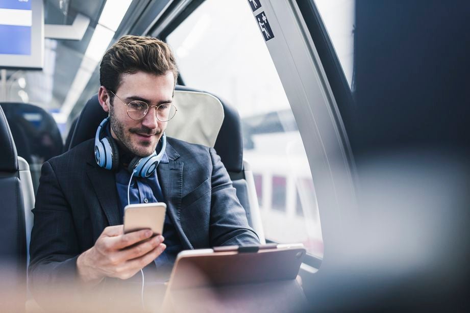 A businessman holding a smartphone while traveling on a train.