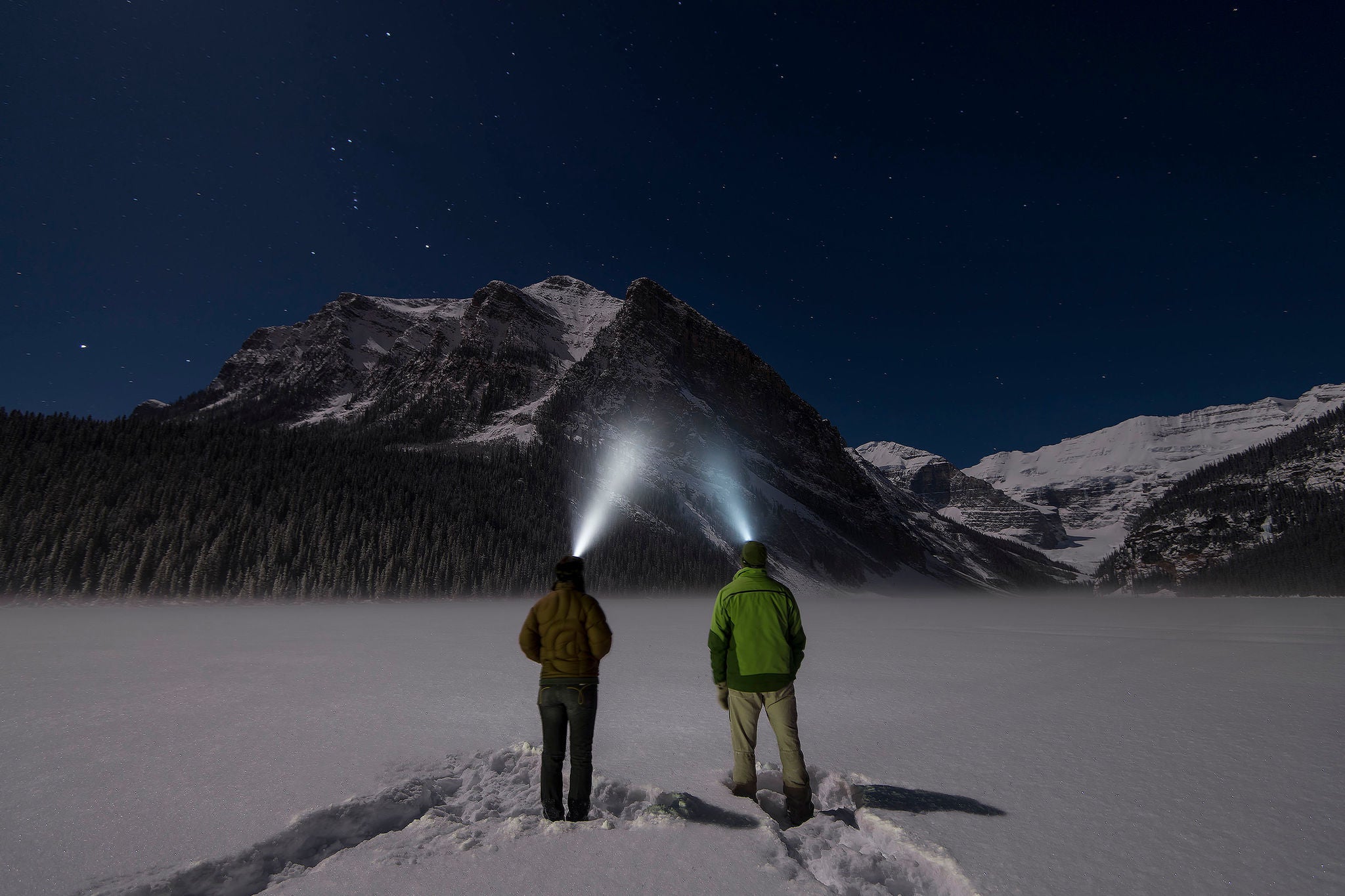 Ey couple stand in snowy clearing with headlamps