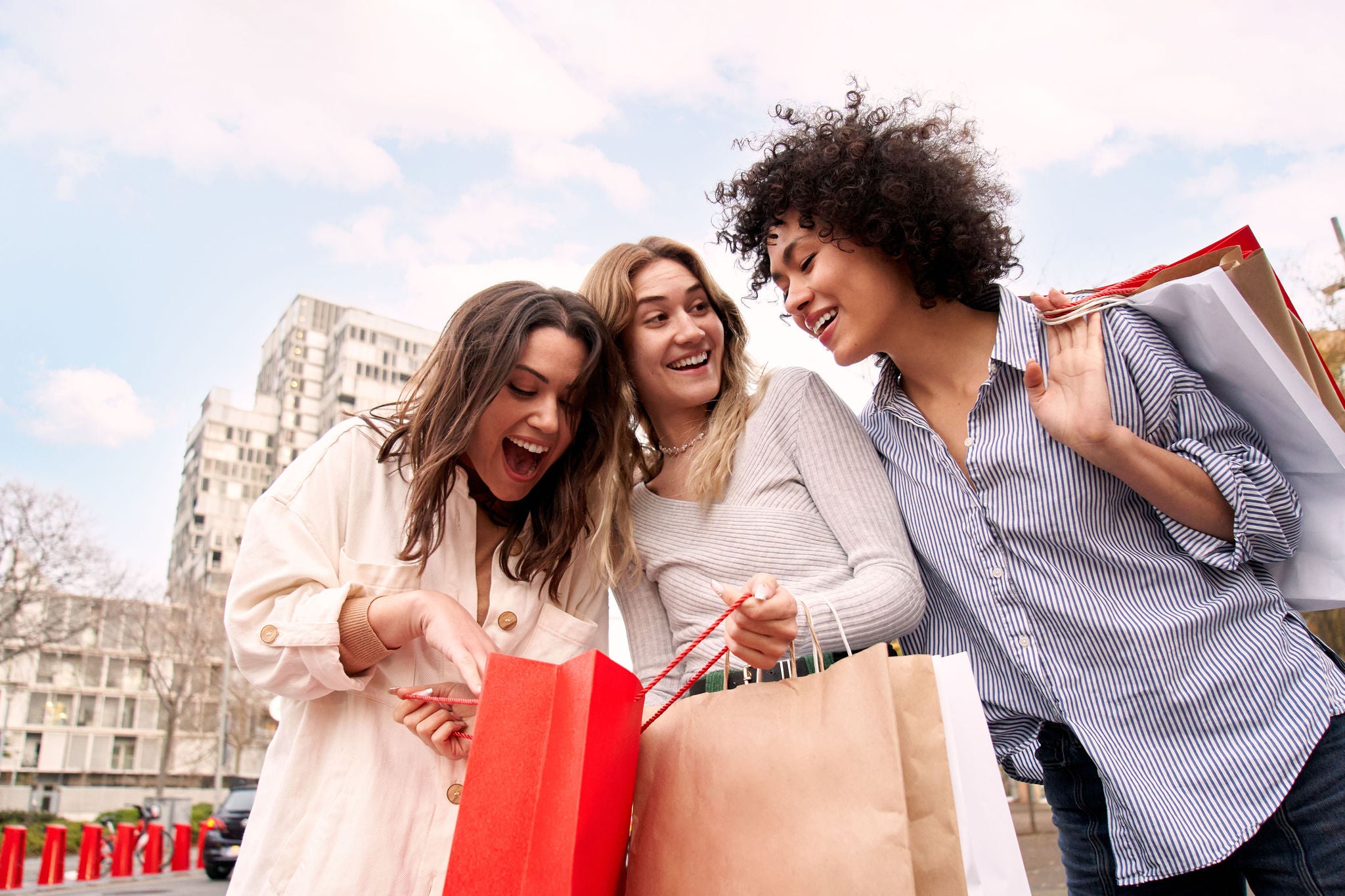 Three enthusiastic European friends on city street hold paper sack