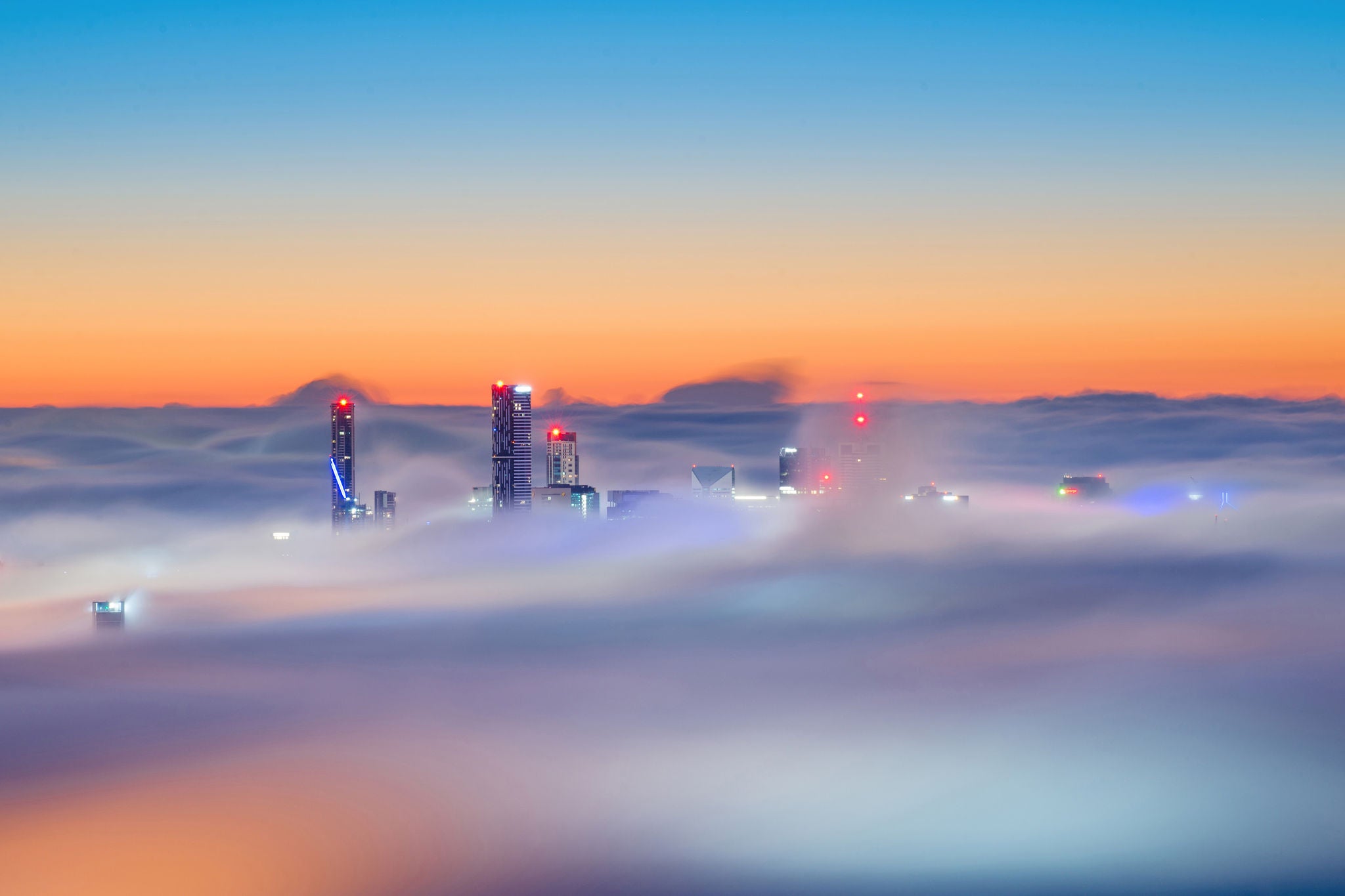 Die Sonne geht am Himmel ueber Brisbane unter, waehrend die Stadt im Nebel liegt.