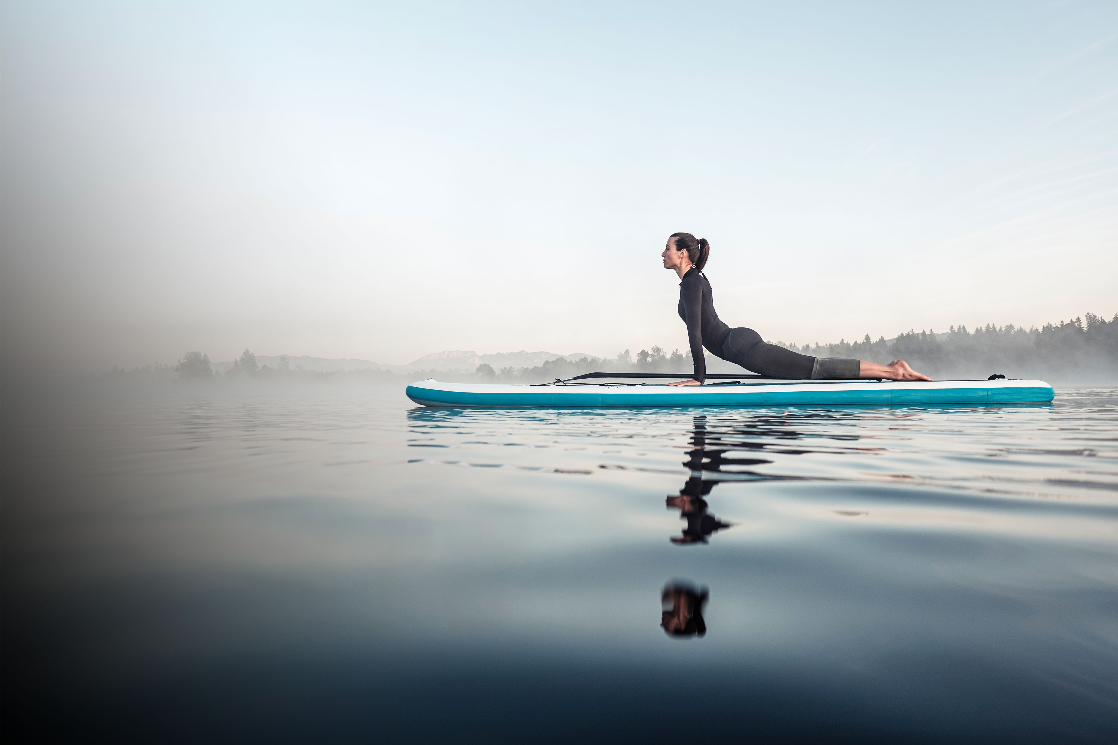 Woman practicing paddle board yoga on lake Kirchsee in the morning Germany, Woman practicing paddle board yoga on lake Kirchsee in the morni