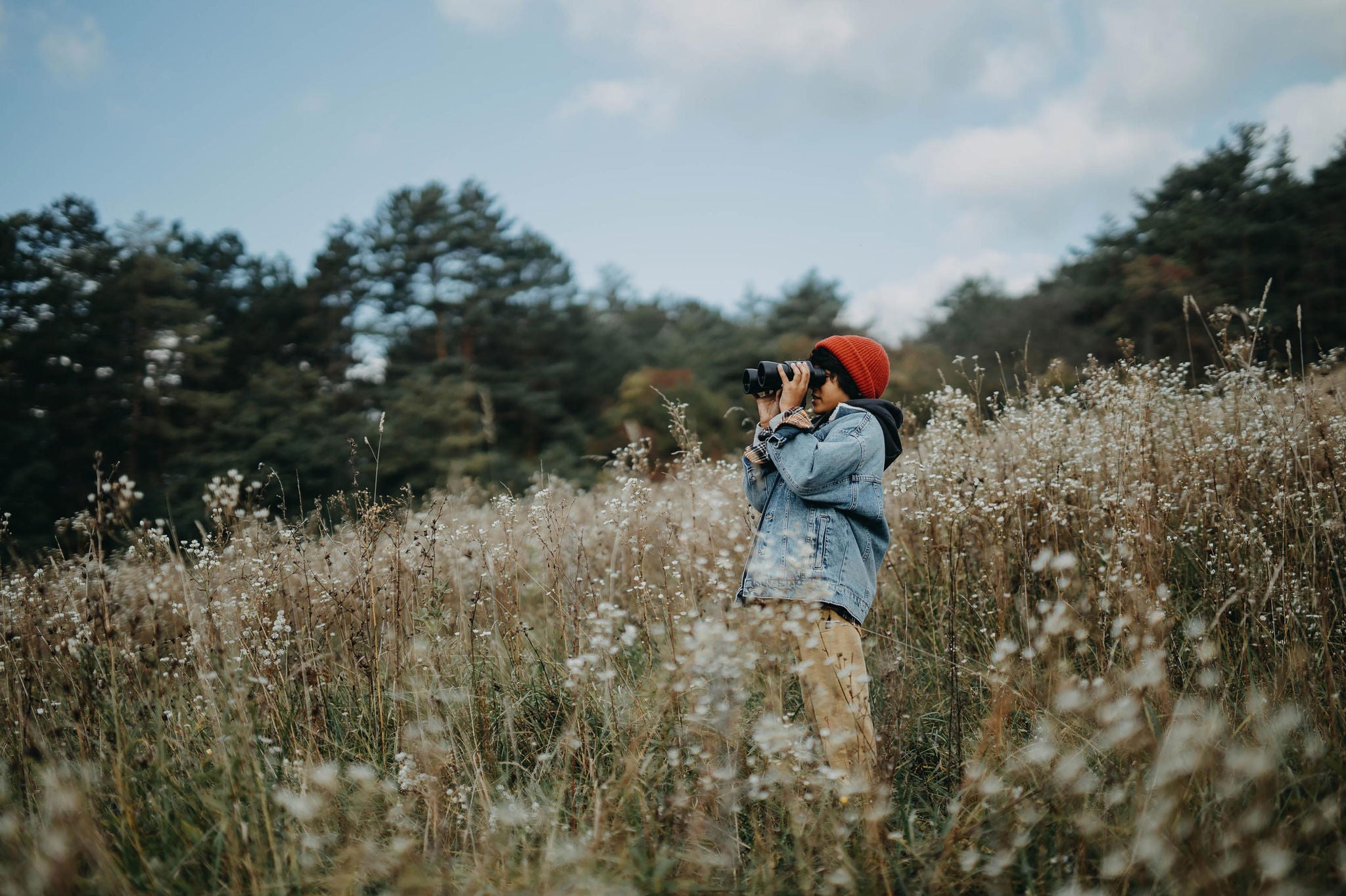 Little Boy standing on a hill and looking through binoculars in autumn day.