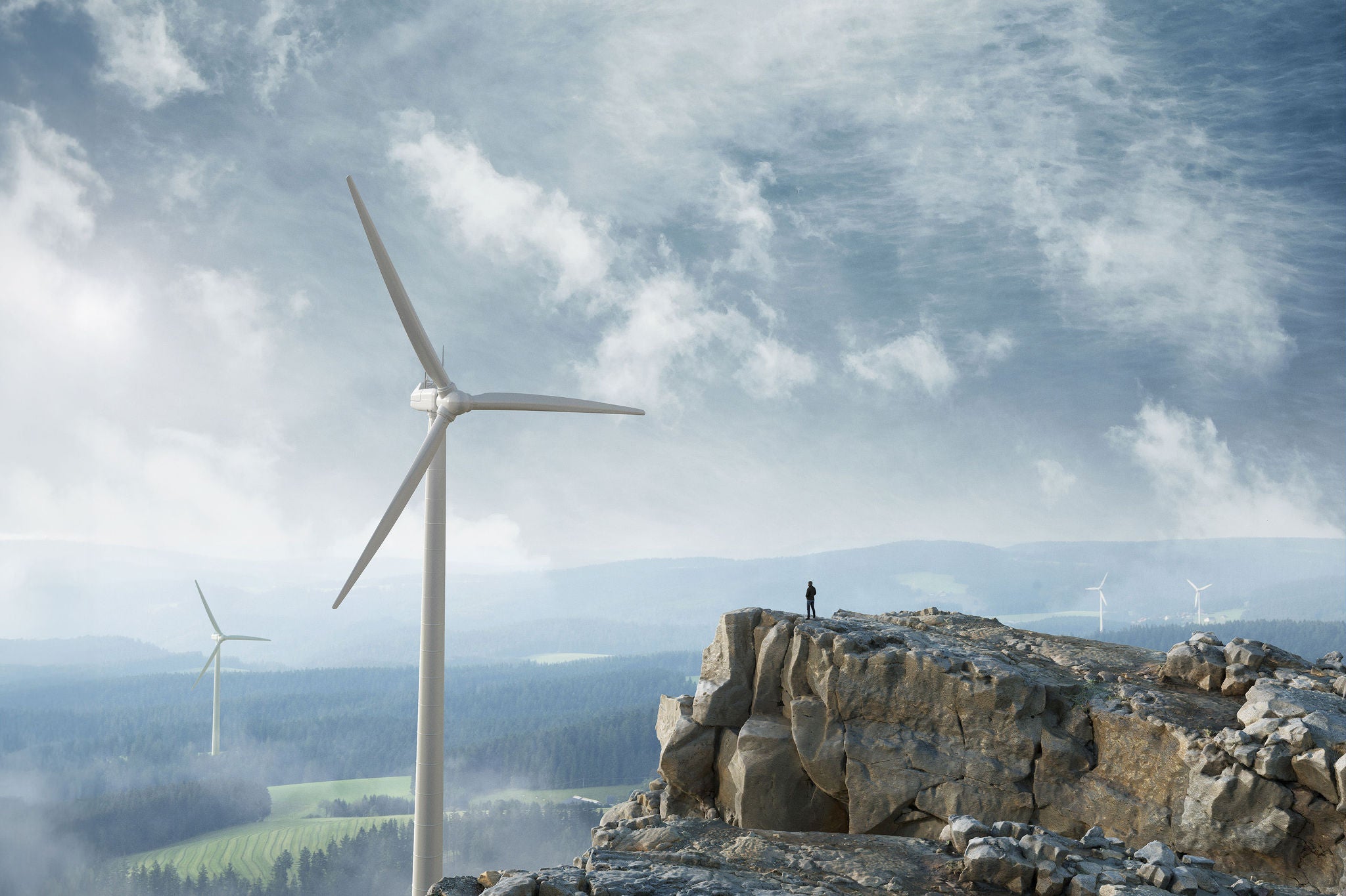 Silhouette eines Mannes auf dem Gipfel einer Klippe mit Blick auf den Horizont mit Windkraftanlagen