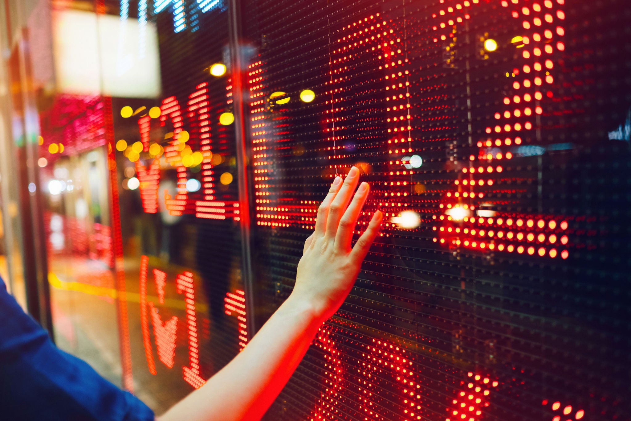 Woman's hand on stock exchange market display screen board on the street showing stock drops in red colour