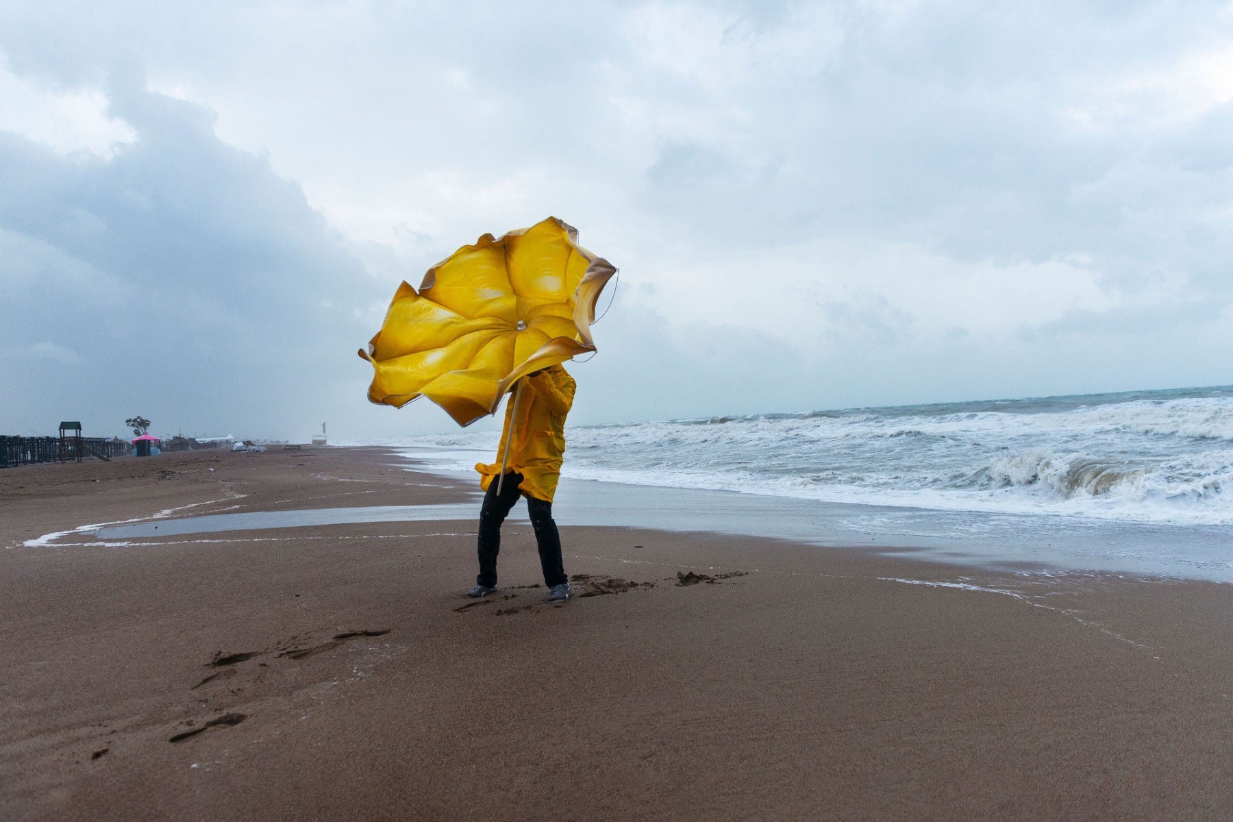 Man on stormy beach with yellow umbrella