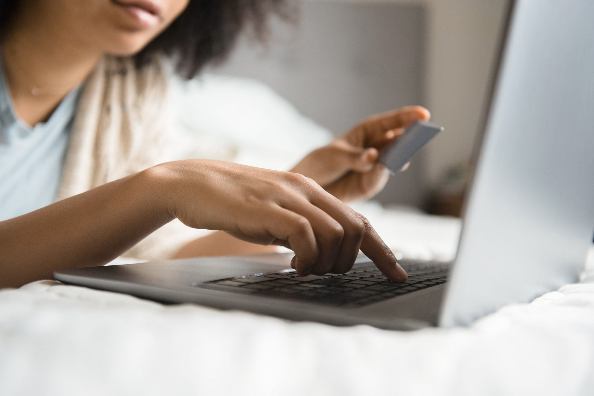 African American woman laying in bed online shopping with laptop