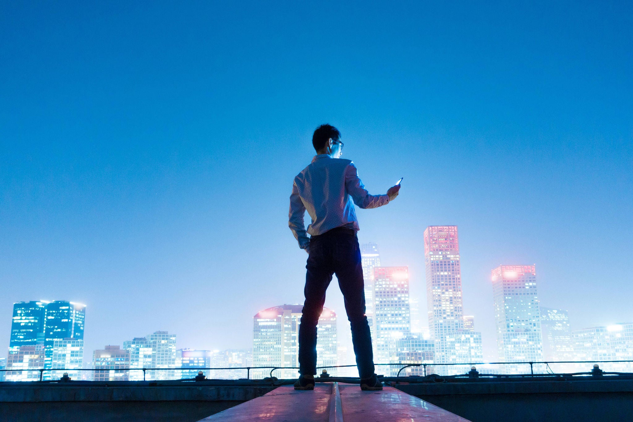 Businessman using smart phone standing on roof with city skyline,Beijing,China