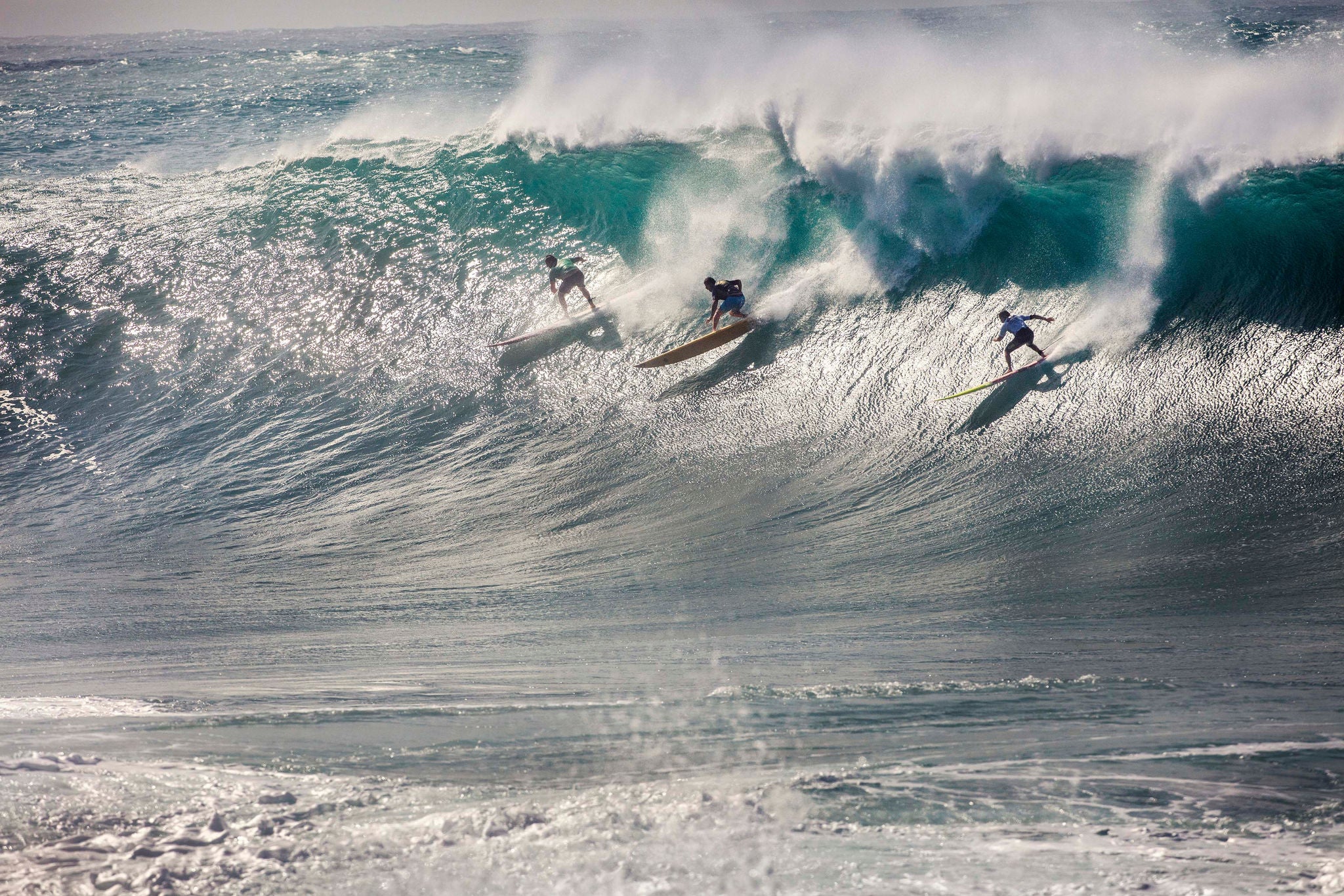 imagem ampla mostra três surfistas surfando a mesma onda.