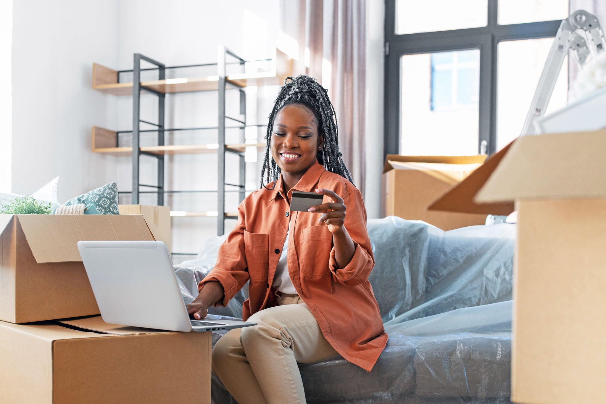 moving, people and real estate concept - happy smiling woman with laptop computer and credit card at new home
