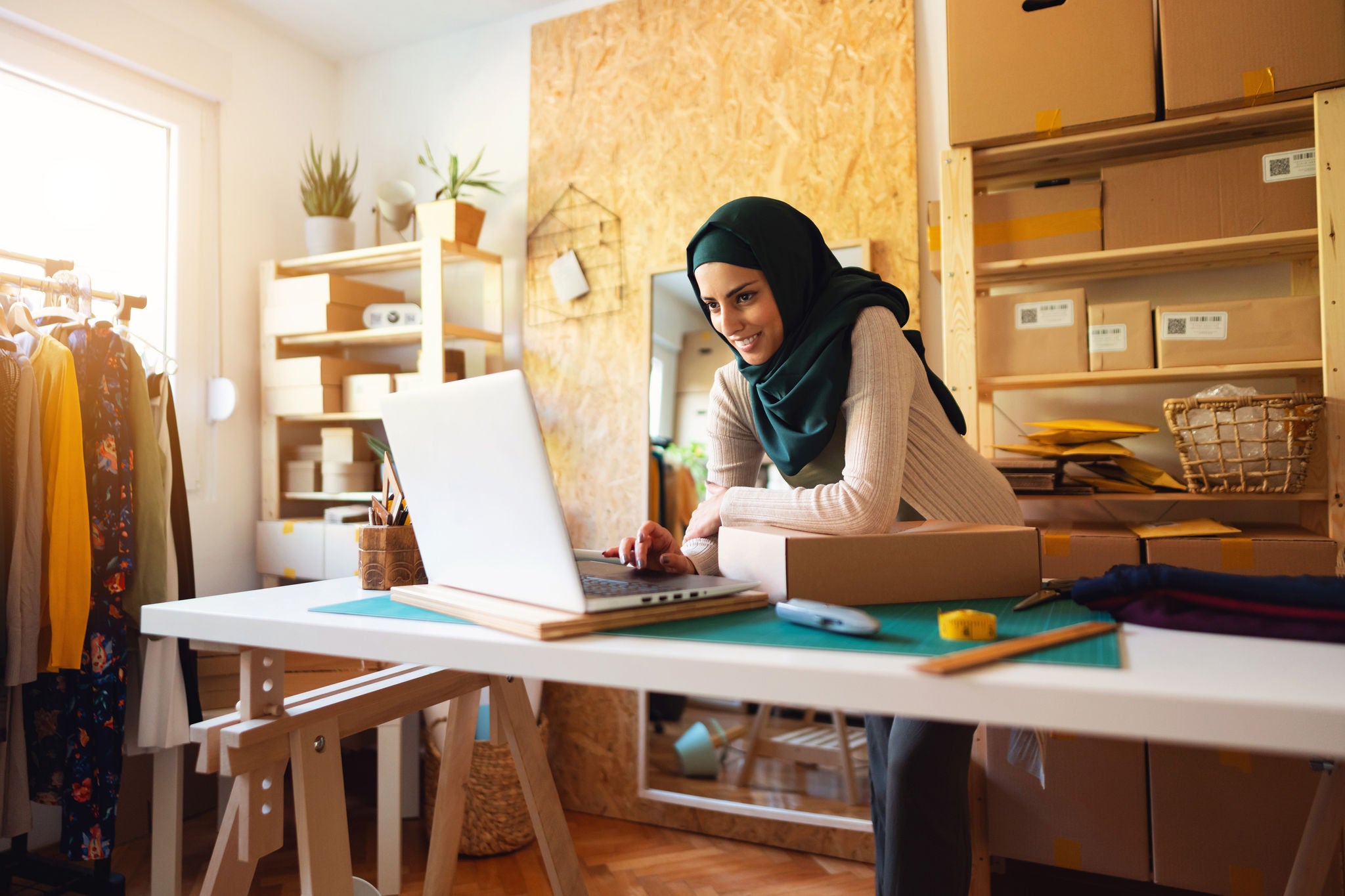 Smiling Muslim businesswoman with hijab using laptop and working e-commerce small business from home.