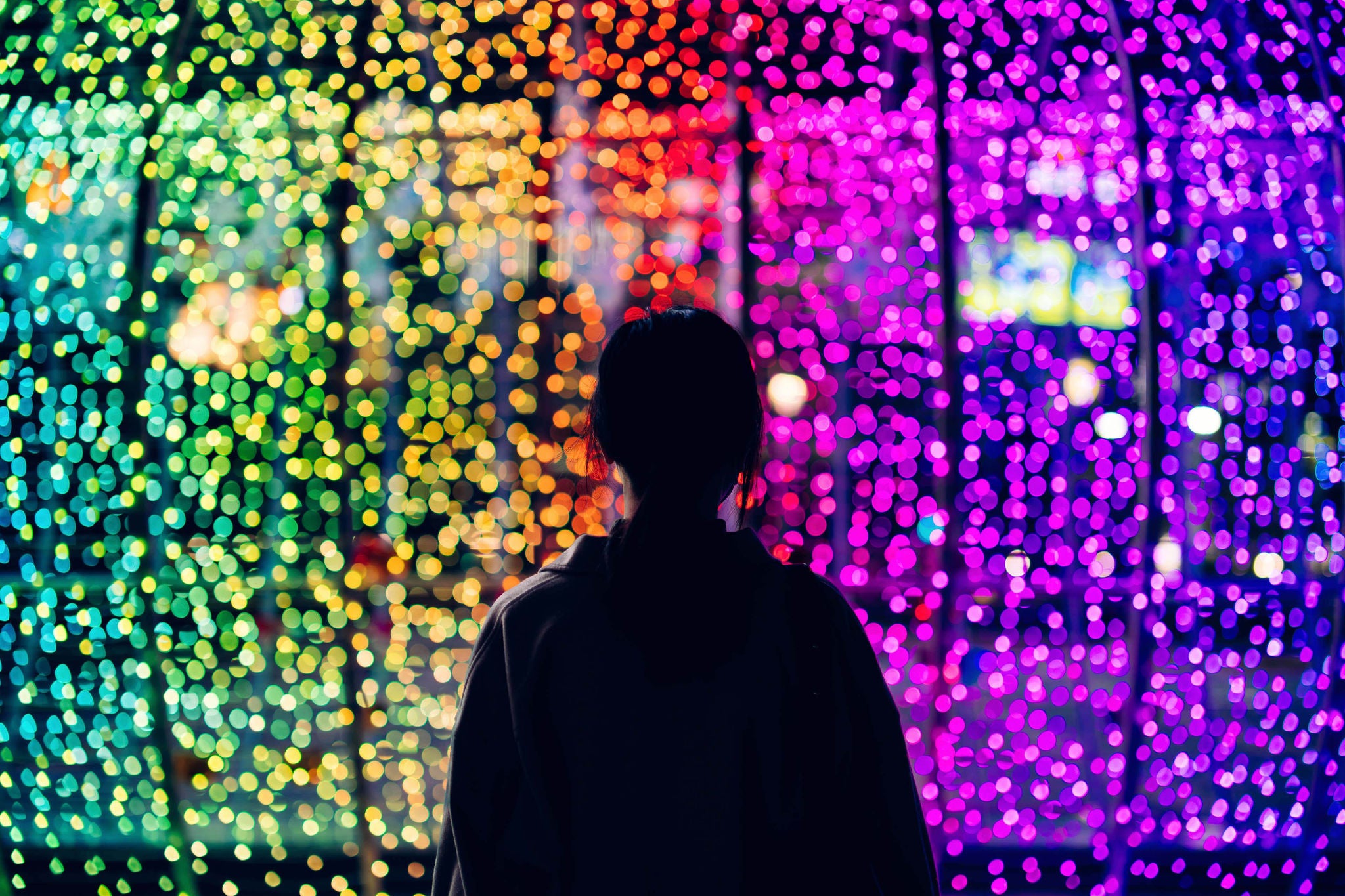 Silhouette of young woman standing against illuminated and colorful bokeh lights