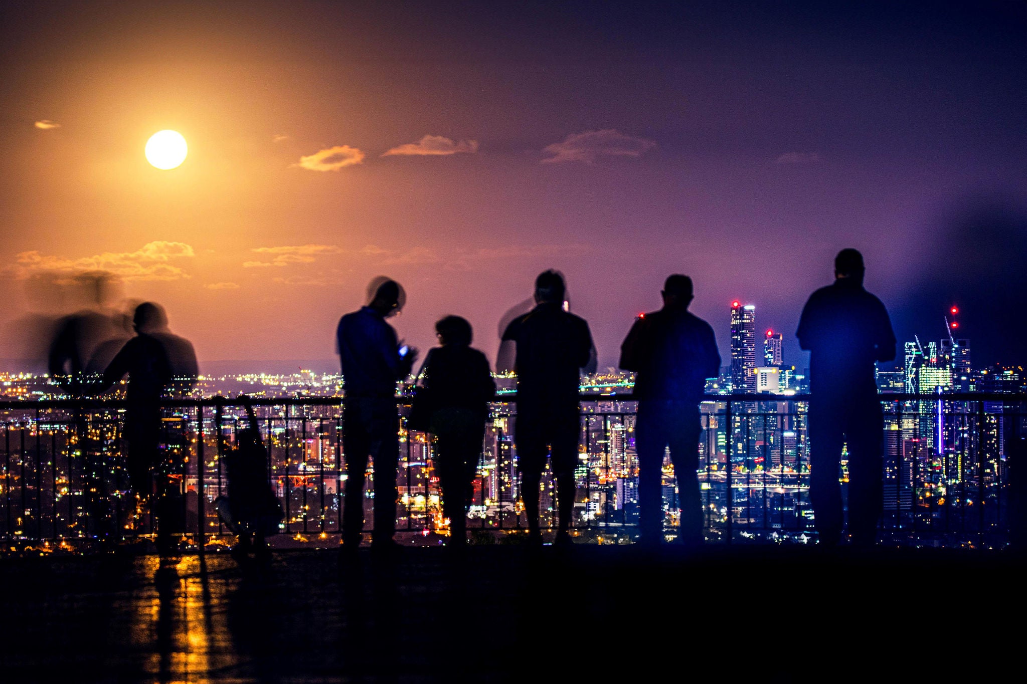 people viewing glowing supermoon in a city at night