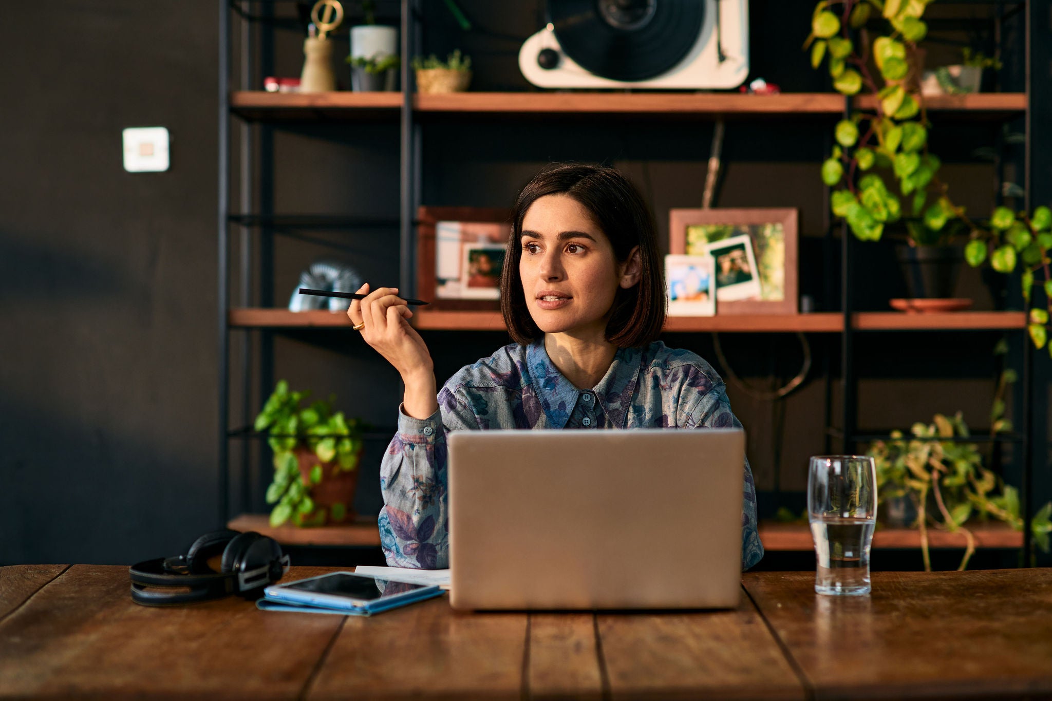 Female entrepreneur remote working, holding pen and contemplating, sitting at table, WFH