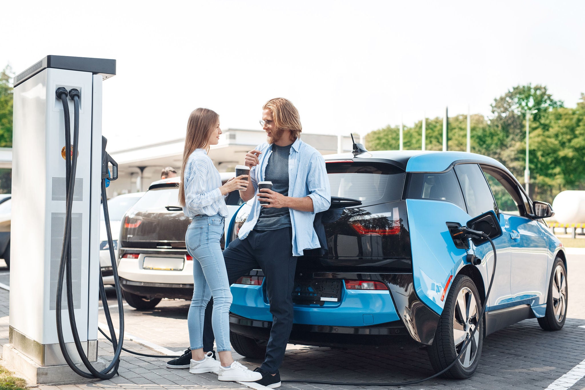 Young couple drinking hot coffee talking smiling happy while waiting vehicle to charge fully