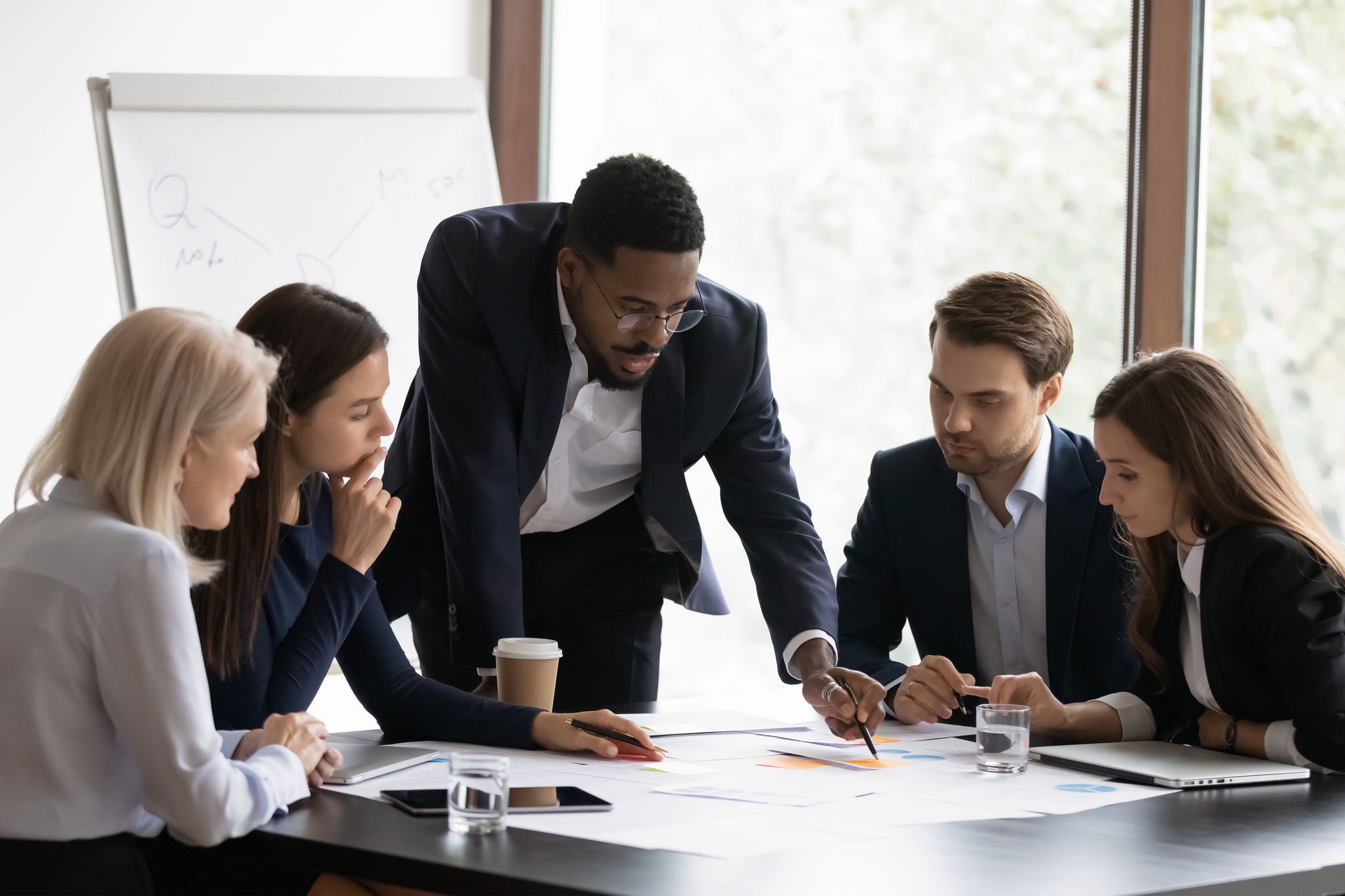 Confident african American male boss work cooperate with diverse team at office briefing, focused biracial businessman head meeting, collaborate discuss business ideas with colleagues at meeting