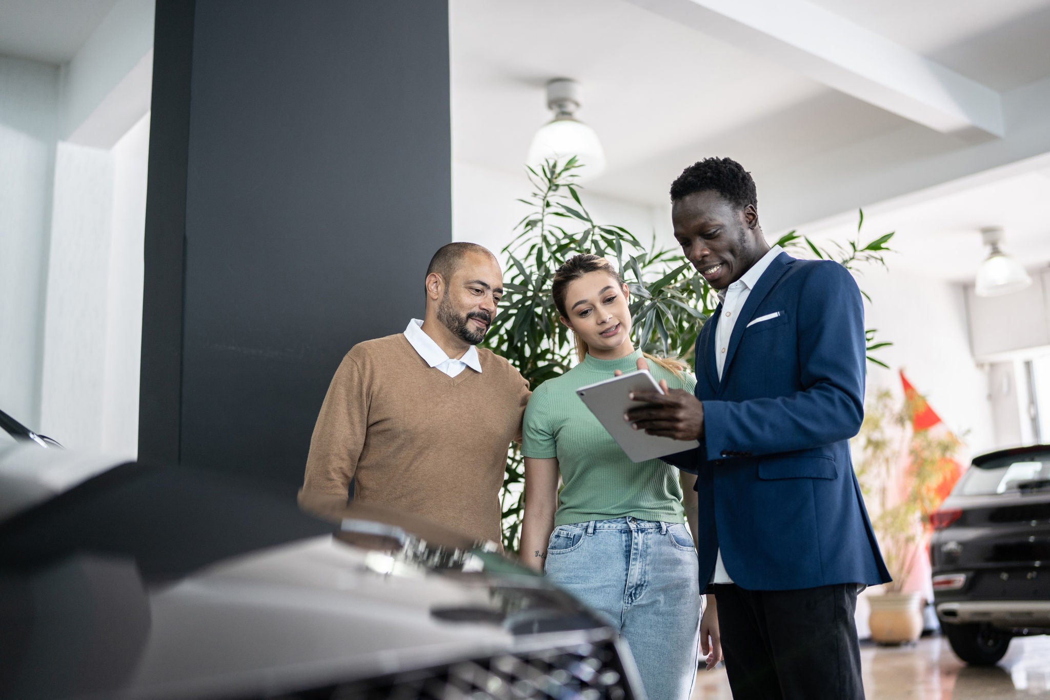 Car salesman discusses new vehicle with customers on tablet