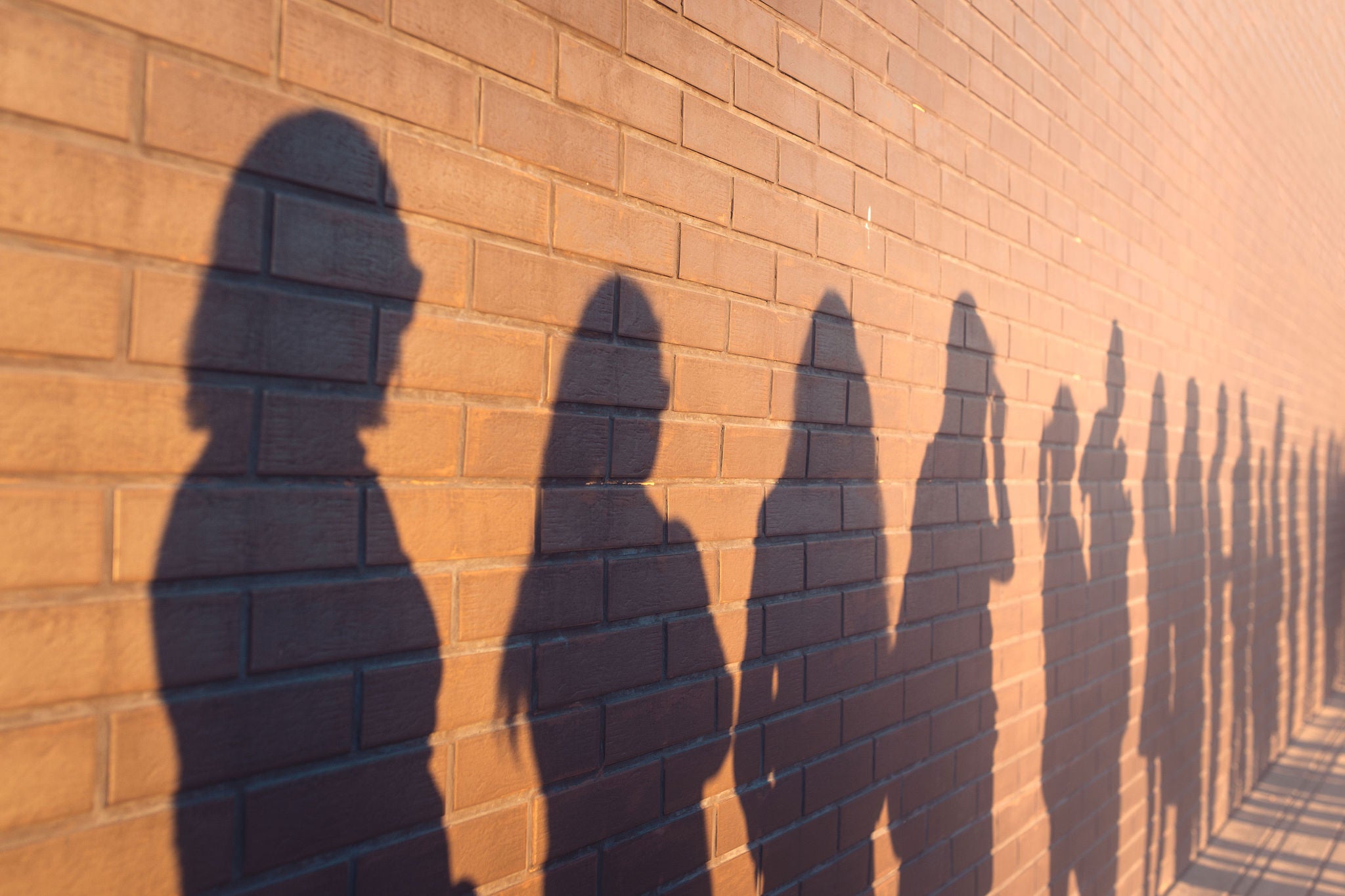 a line of shadows of people lined up against a red brick wall. Stand in a queue to the changes.