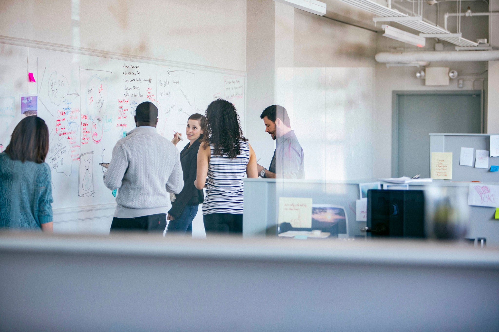 Businesswoman explaining to colleagues by whiteboard seen through glass