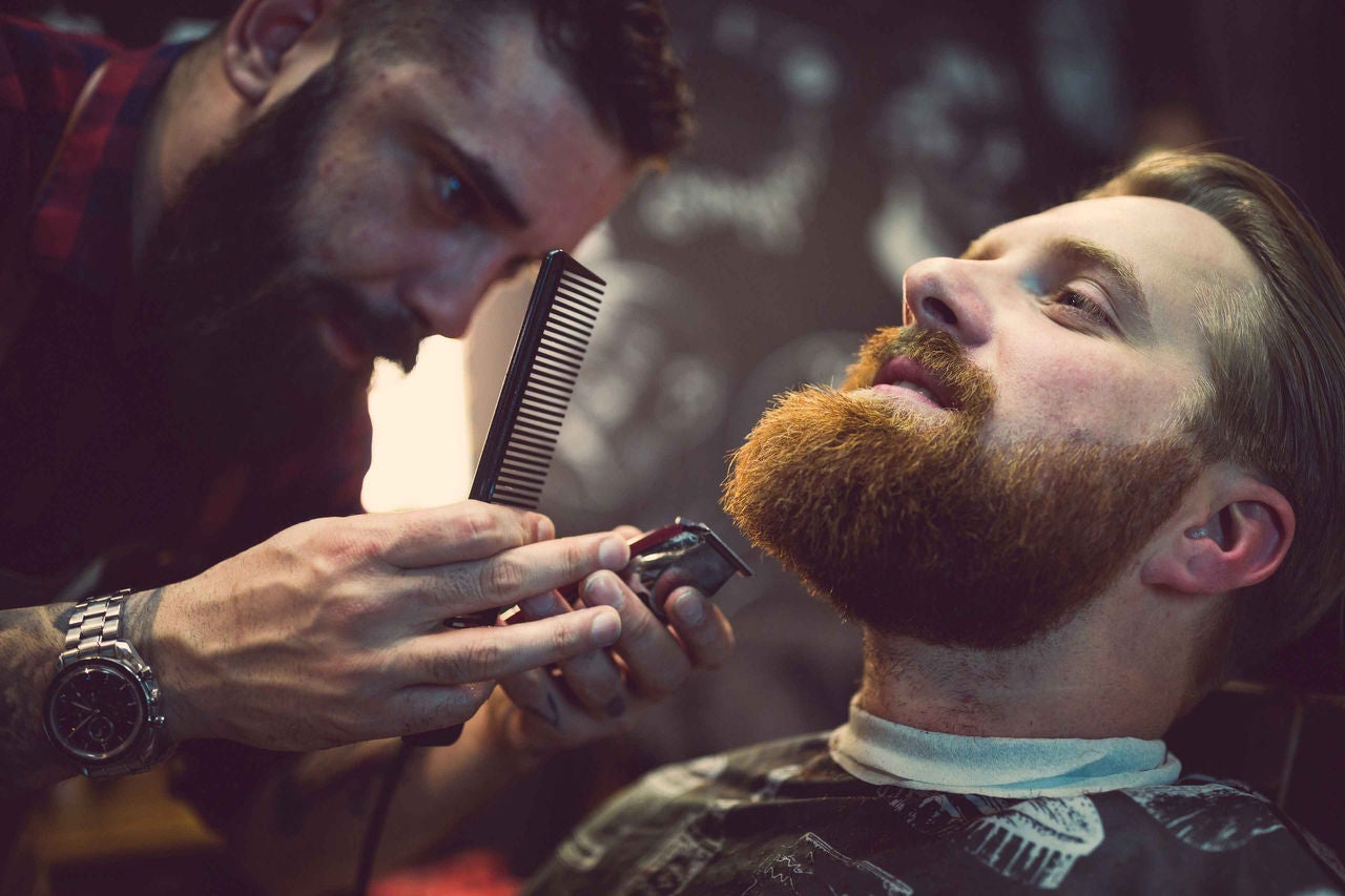 Barbier trimmt Bart eines bÃ¤rtigen Mannes im Barbershop