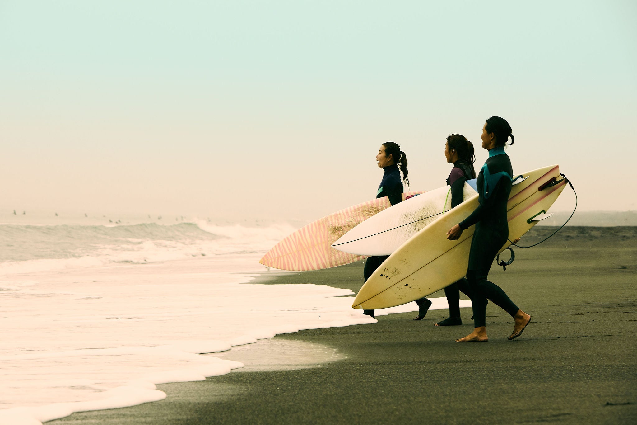 Women's surfers walk towards the sea on a rainy day on Shonan Coast of Japan