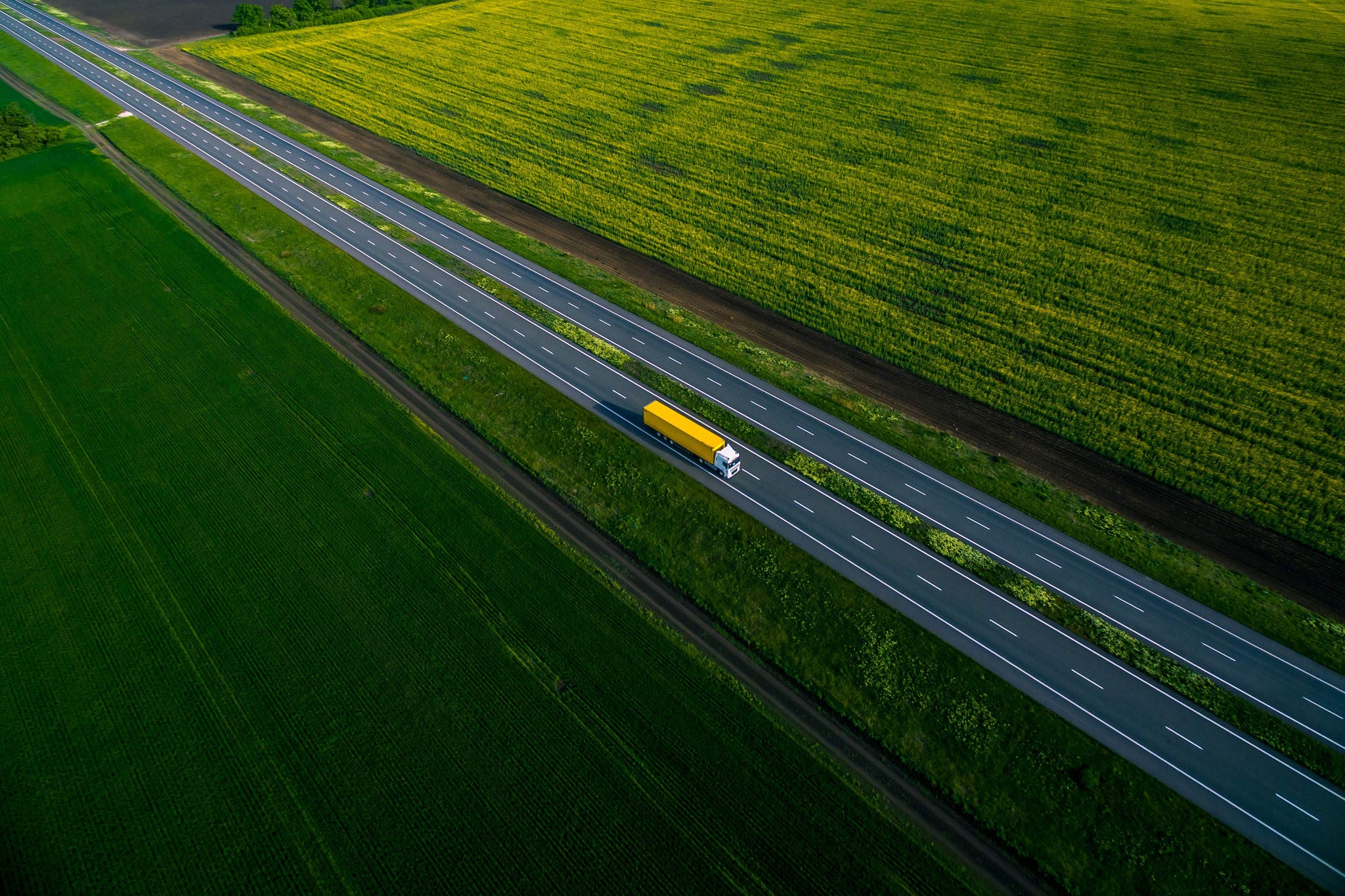 Yellow truck driving on a high way between two fields