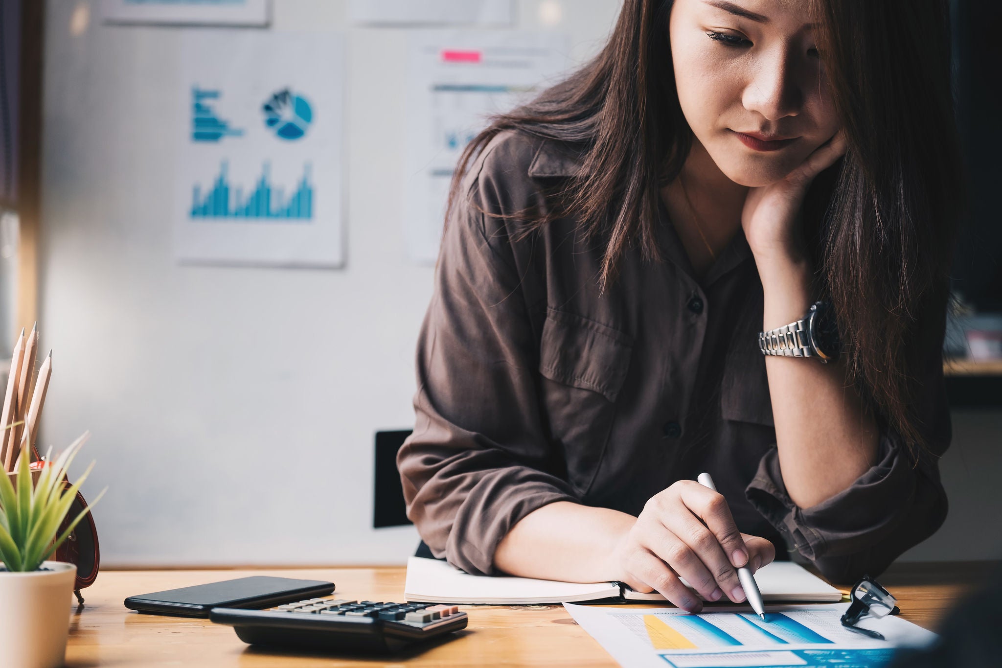 Business woman usinEn kvinna arbetar vid datorn, antecknar och räknar på miniräknare.g calculator