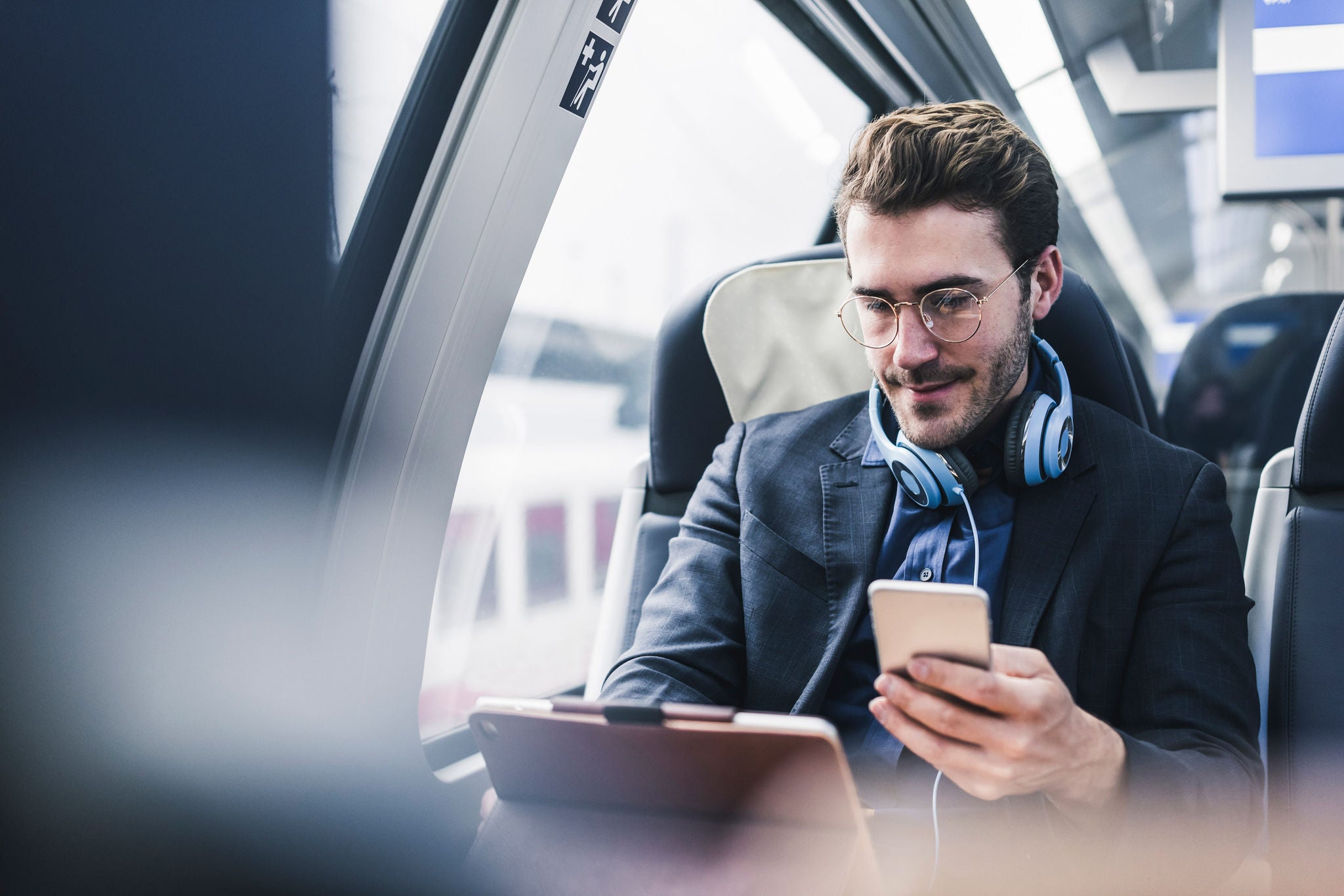 EY Man looking at phone and tablet on train