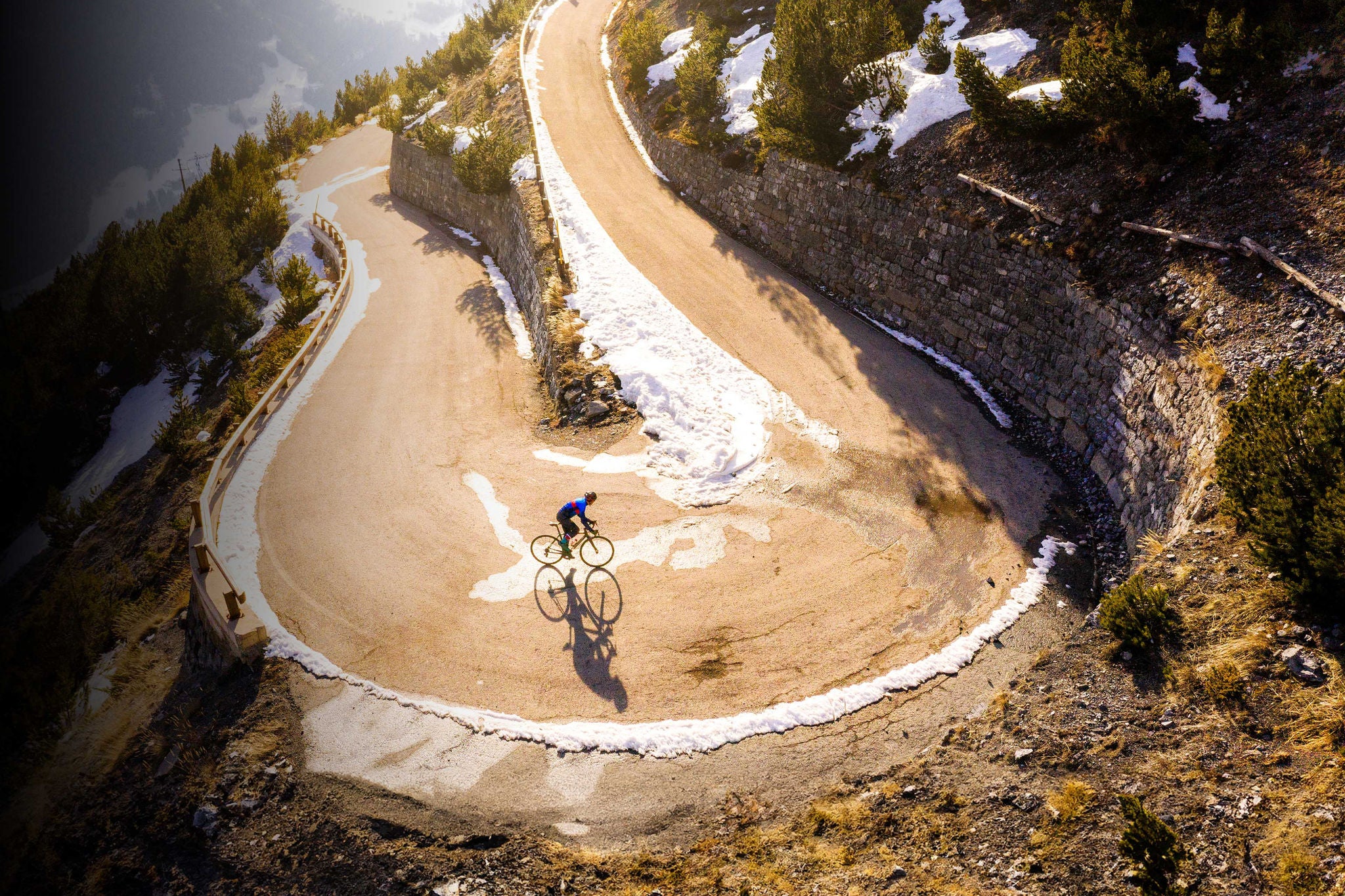 Road cyclist climbing hairpin bends up mountain pass in winter with snow. Cancano, Bormio, Valtellina, Stelvio National Park, Italy, Europe.