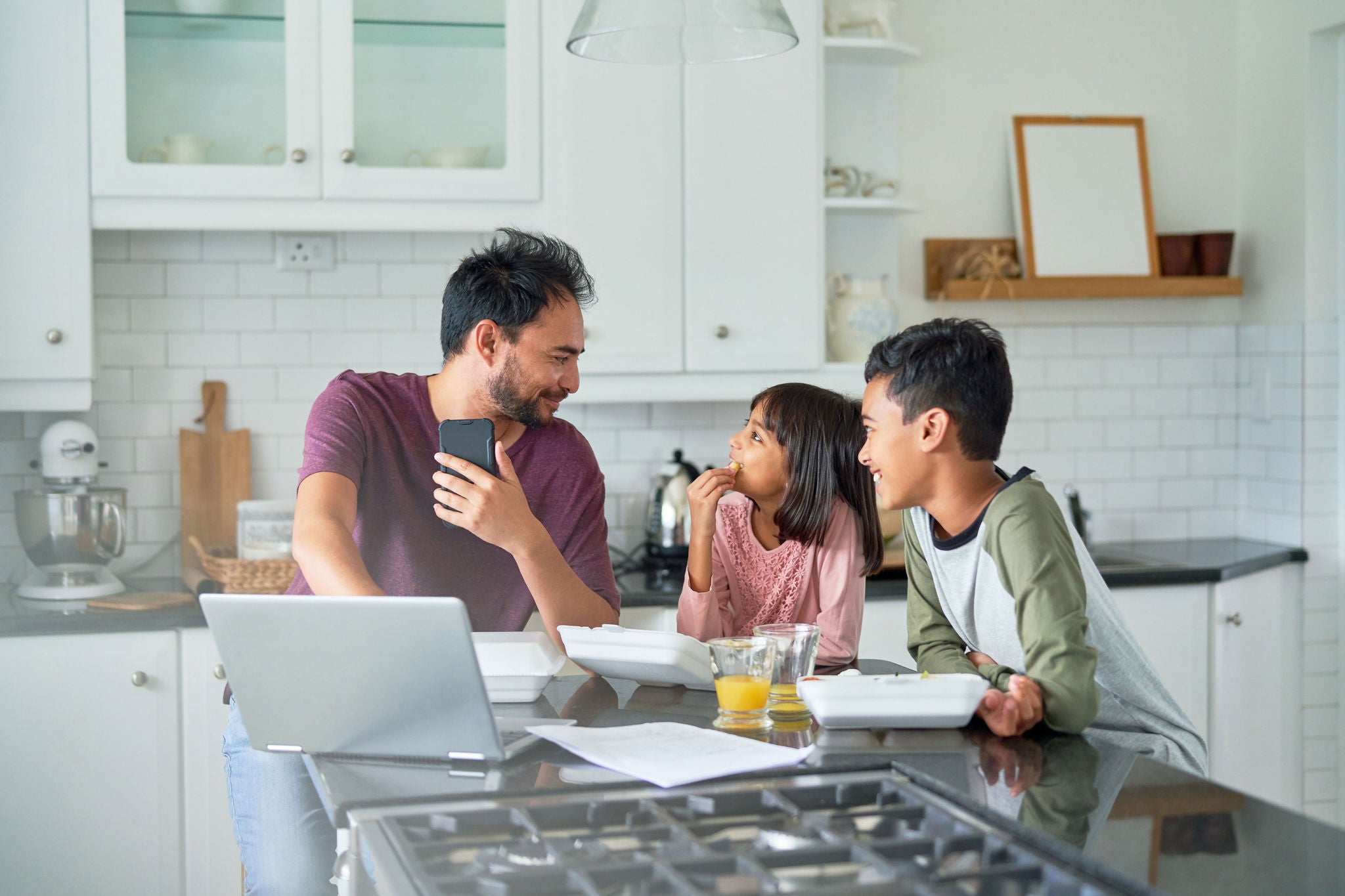 Father working in kitchen with kids eating takeout food