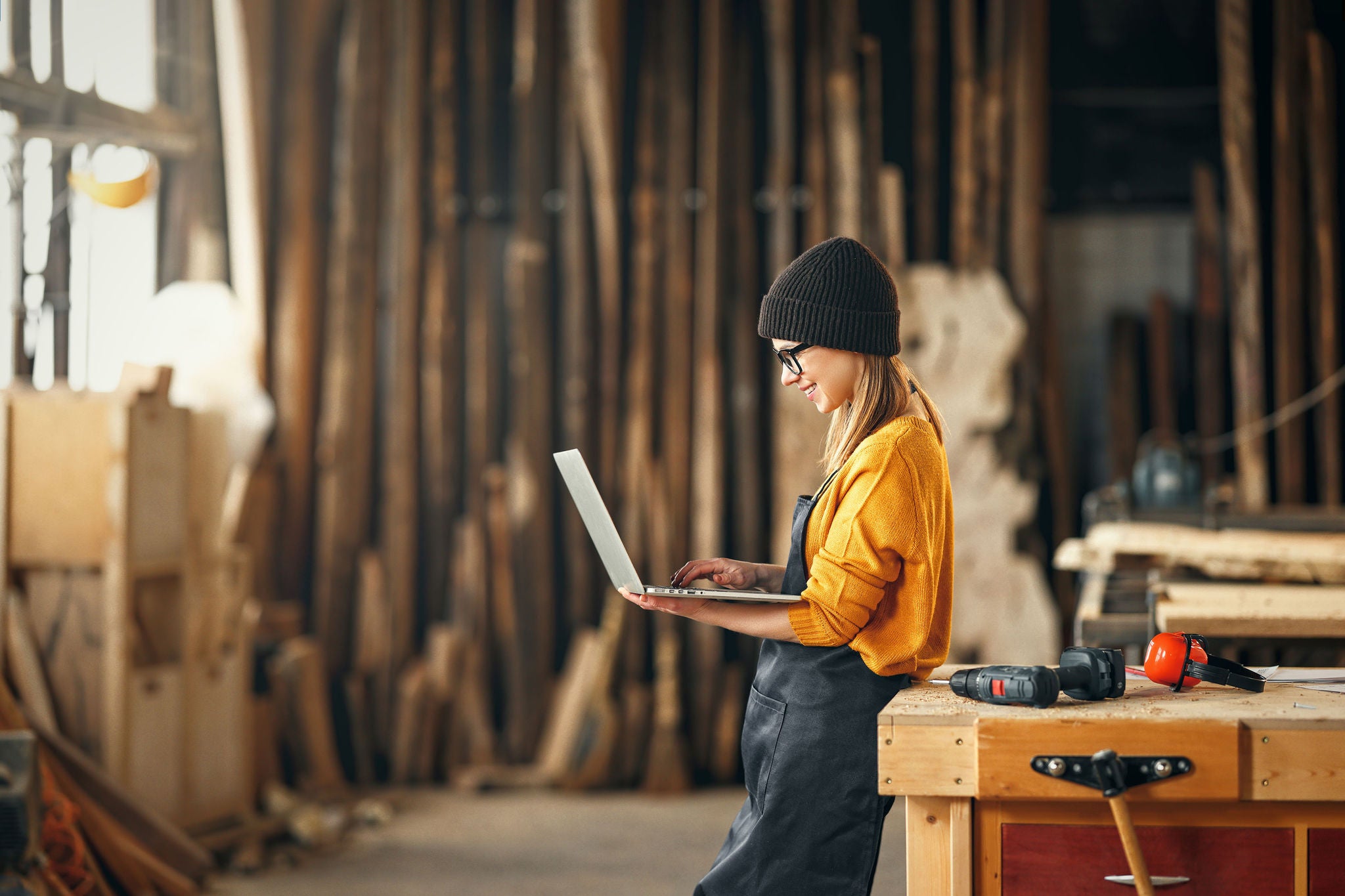 young female carpenter looks drawings on a laptop during  while  break in working with wood in modern handicraft studio