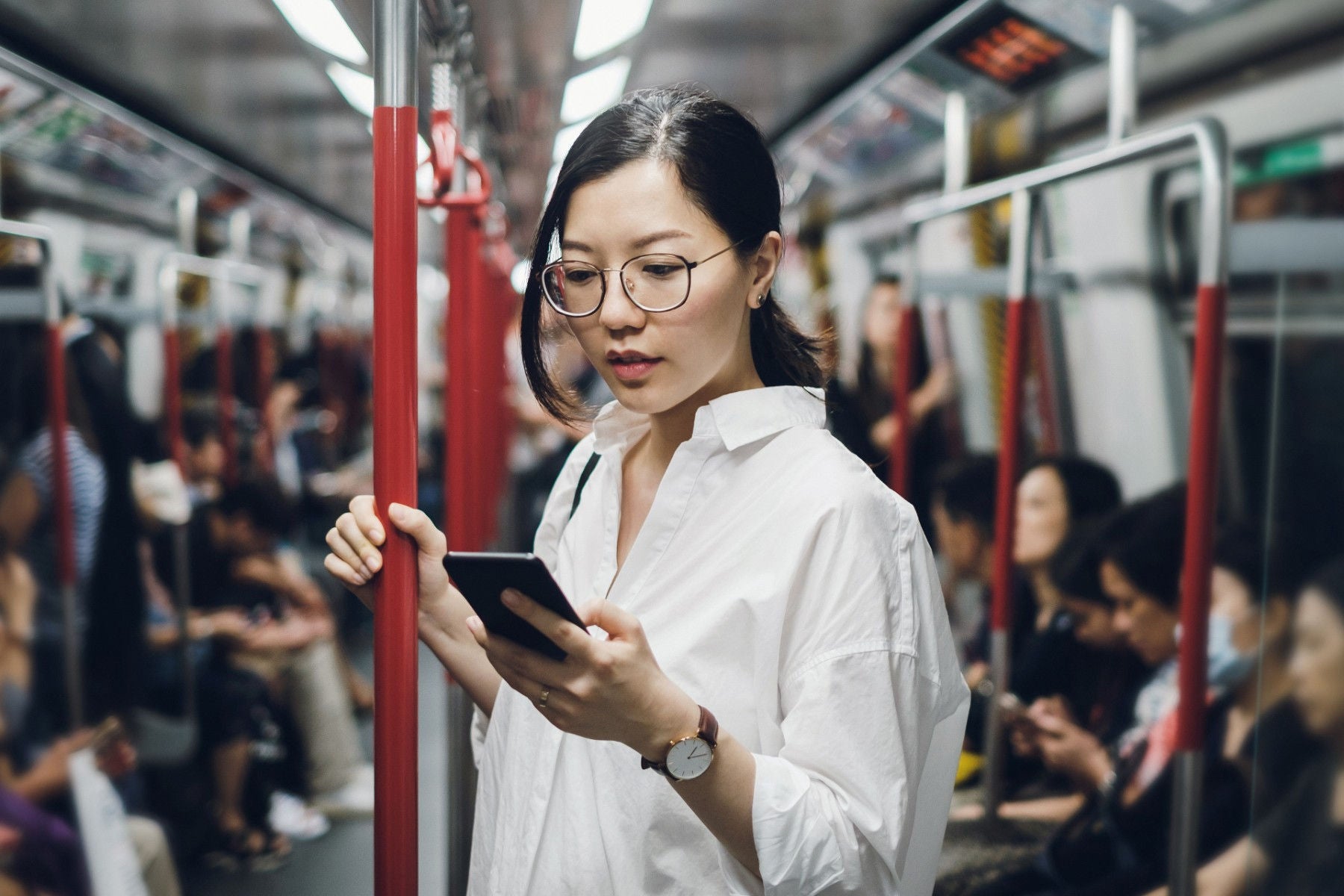 ey asian woman in glasses checks phone on commute