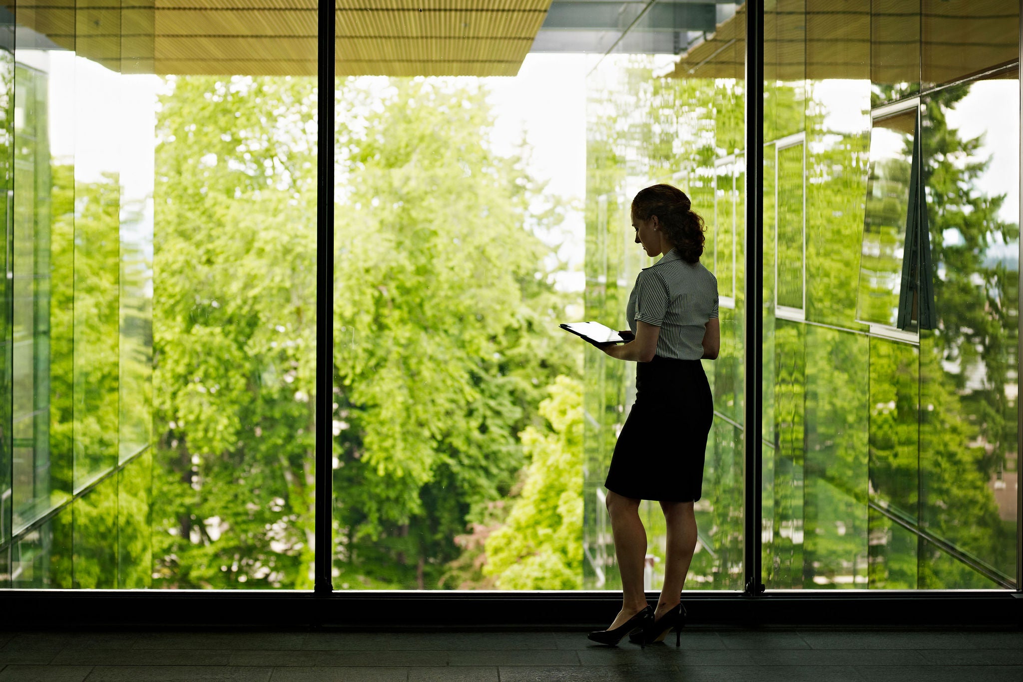 Businesswoman holding tablet standing at glass wall overlooking green space