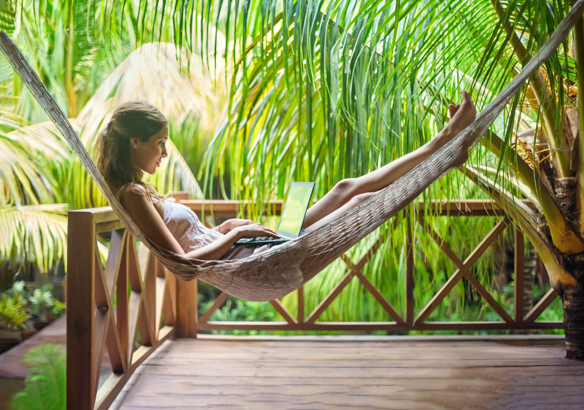 Young beautiful woman lying in a hammock with laptop in a tropical resort